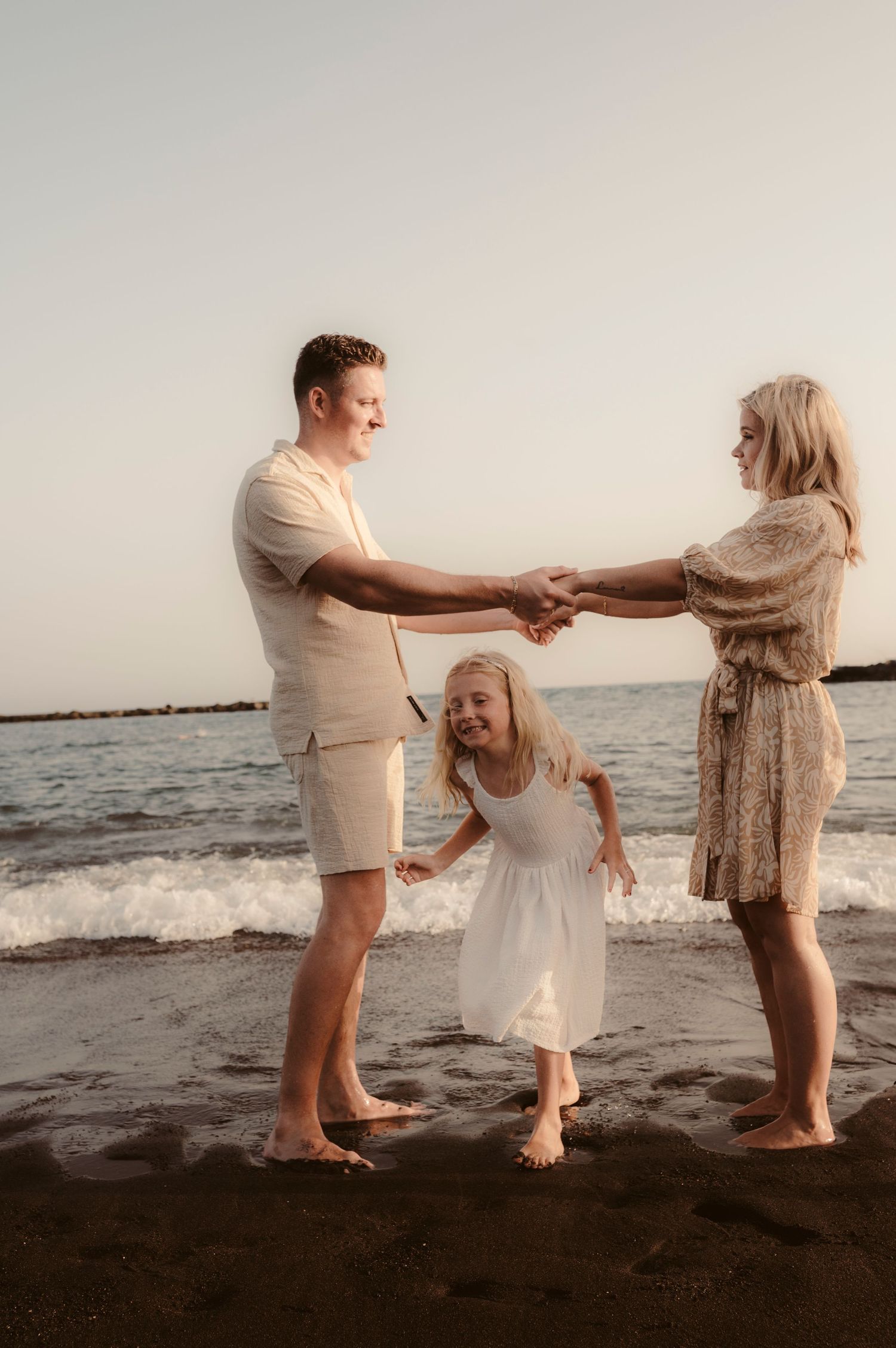 Parents holding hands wide as daughter runs under them on black sand beach