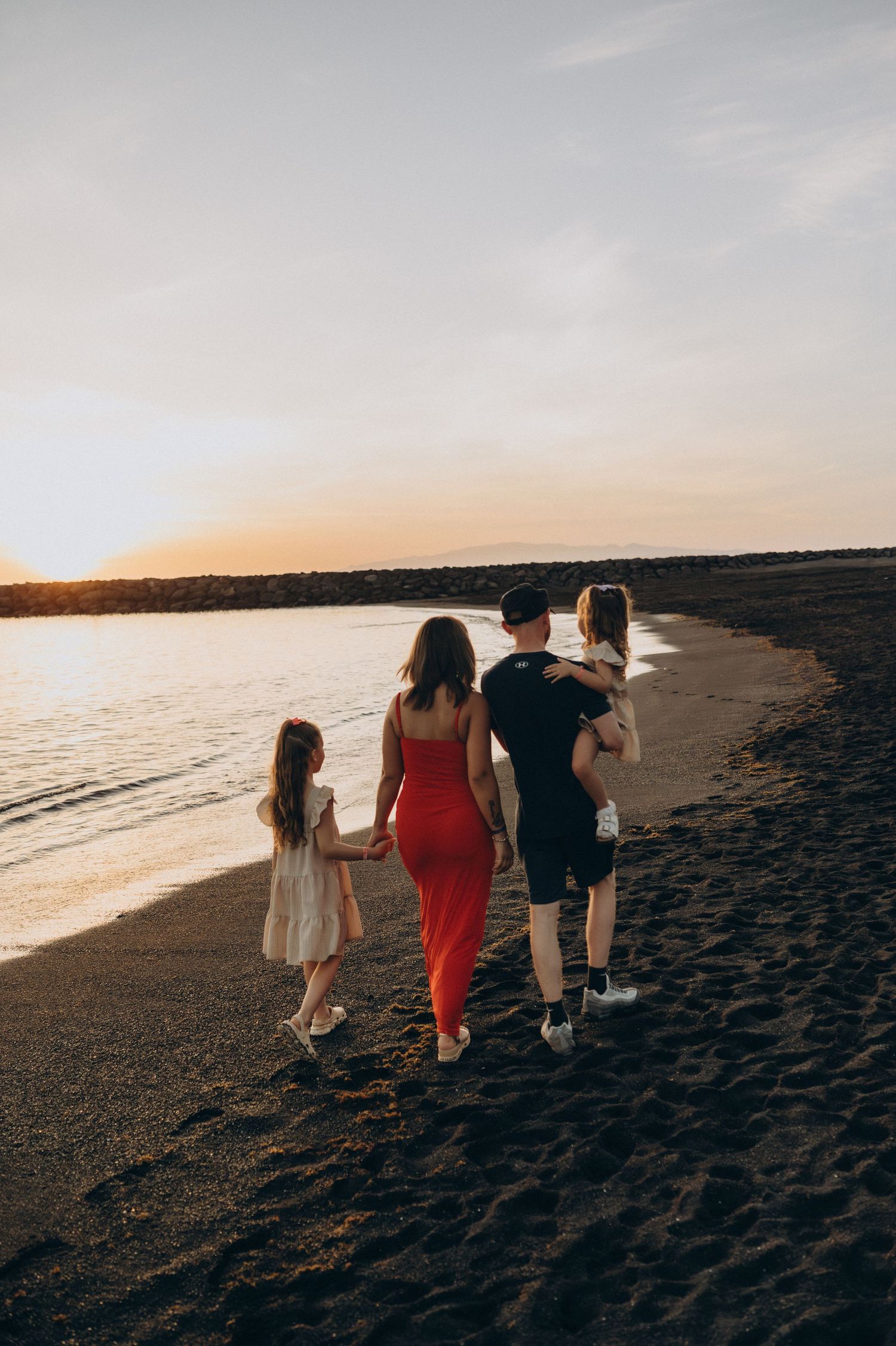 Family walking together along the ocean at sunset on the volcanic beach of Playa del Duque