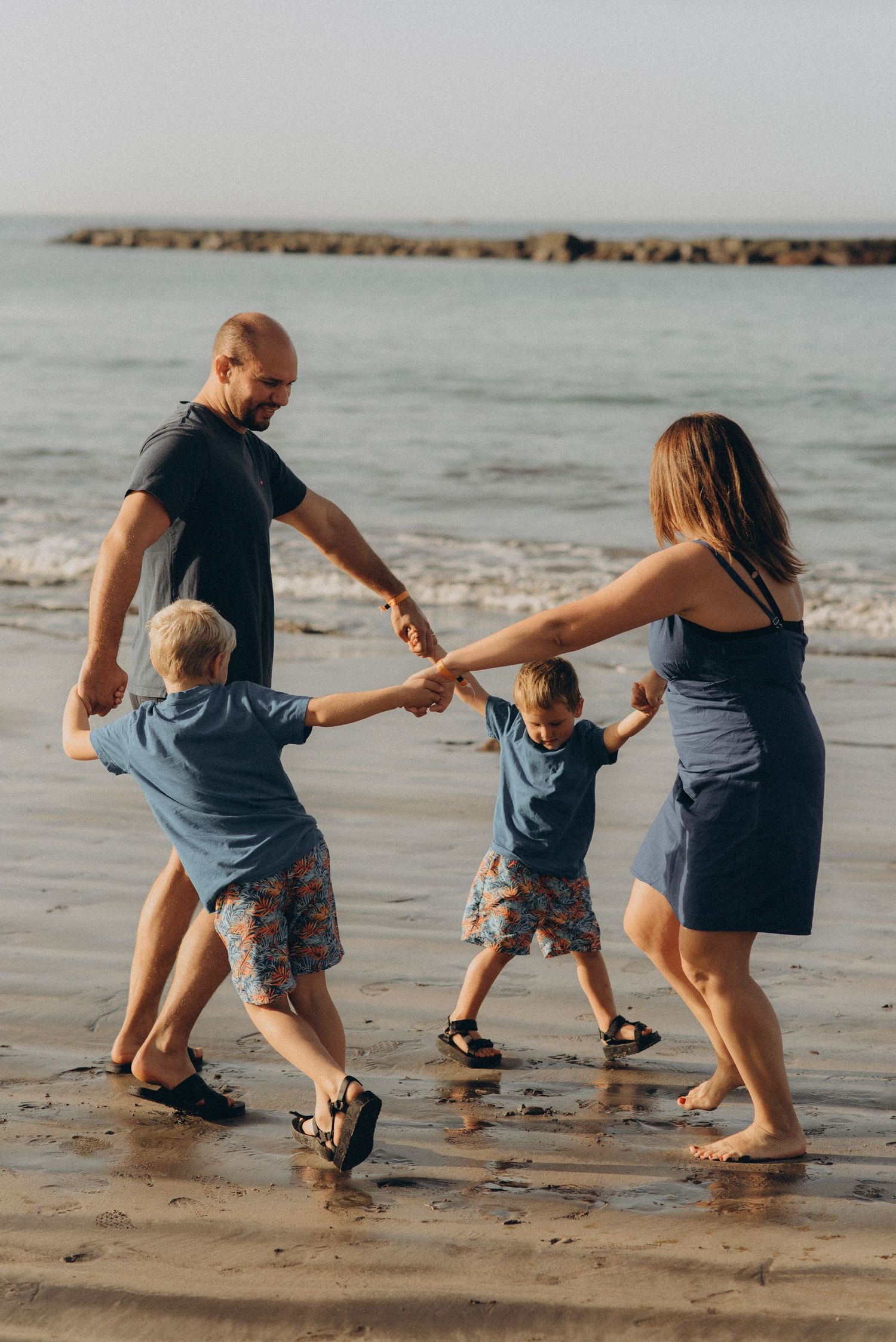 Family holding hands in a circle, twirling and enjoying playful moments together at Playa Fañabé