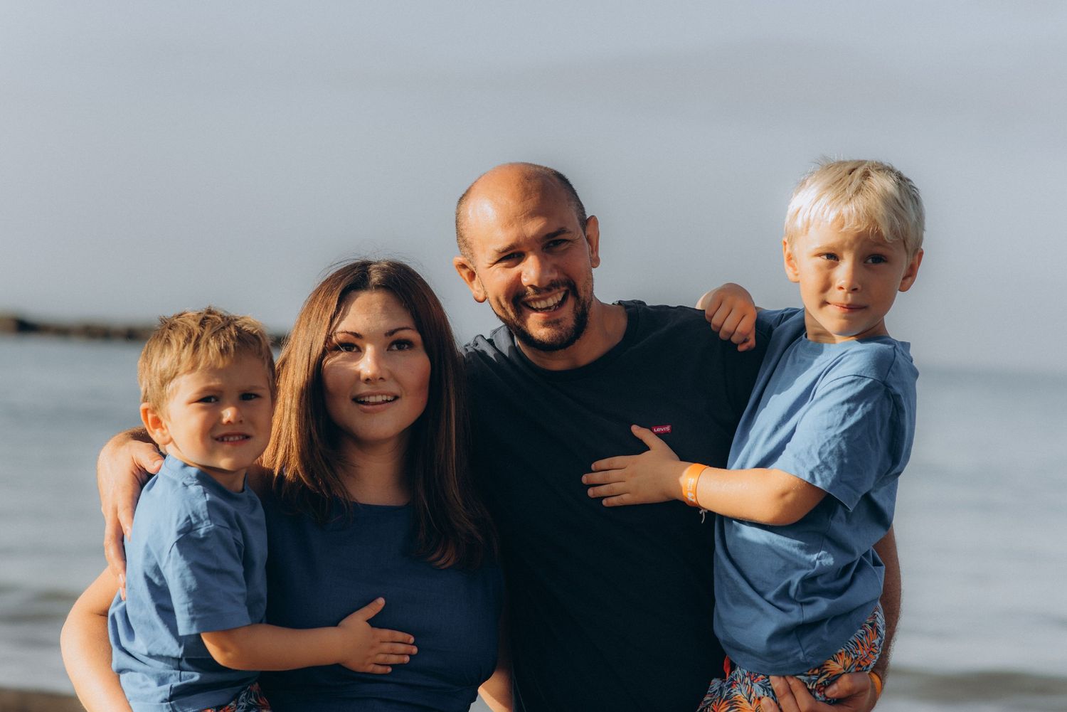 Family of four looking at the camera with boys in parents’ arms in soft Tenerife morning light