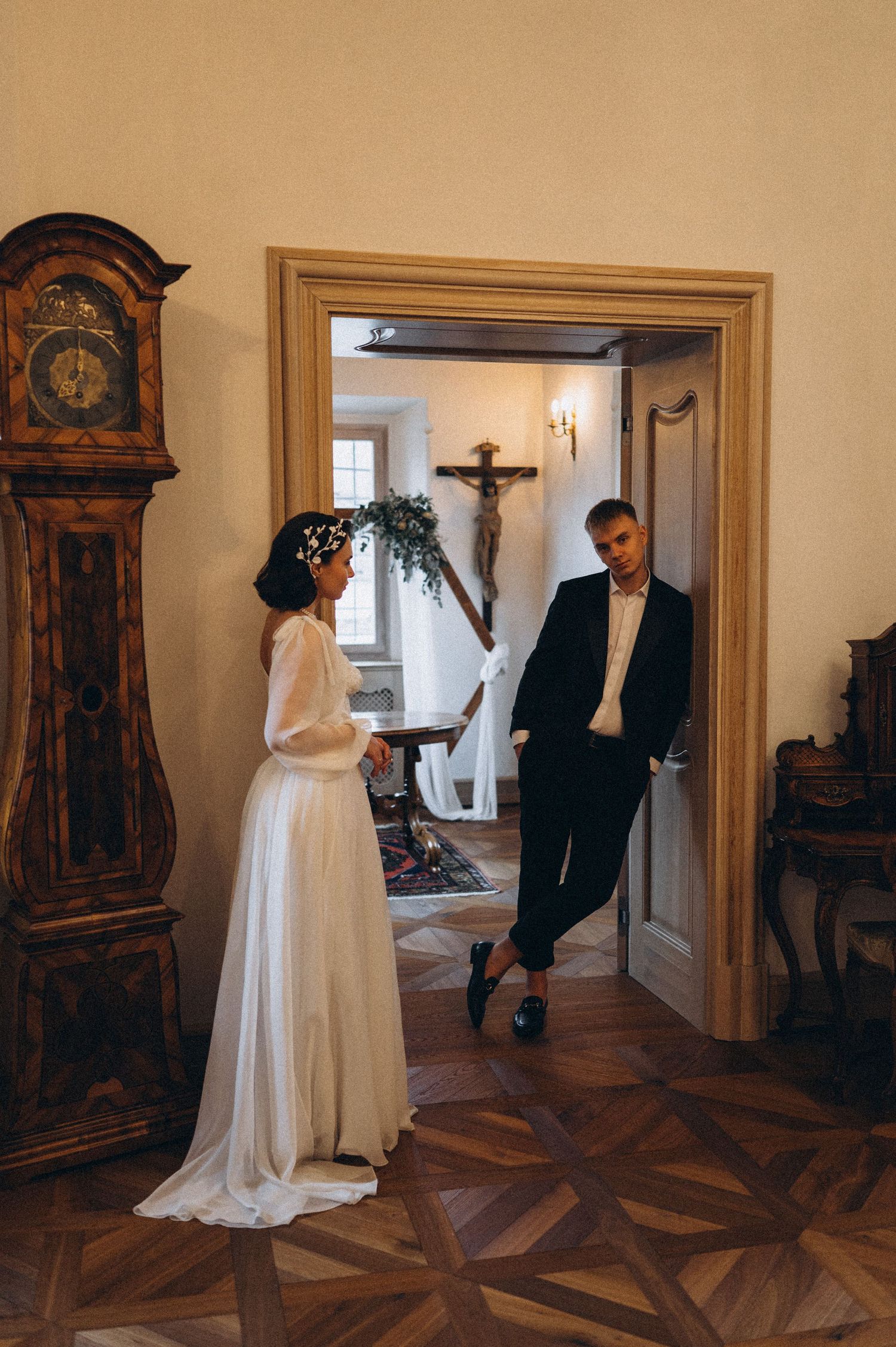 Bride and groom separated by a doorway, sharing a tender and flirtatious look during their wedding photoshoot.