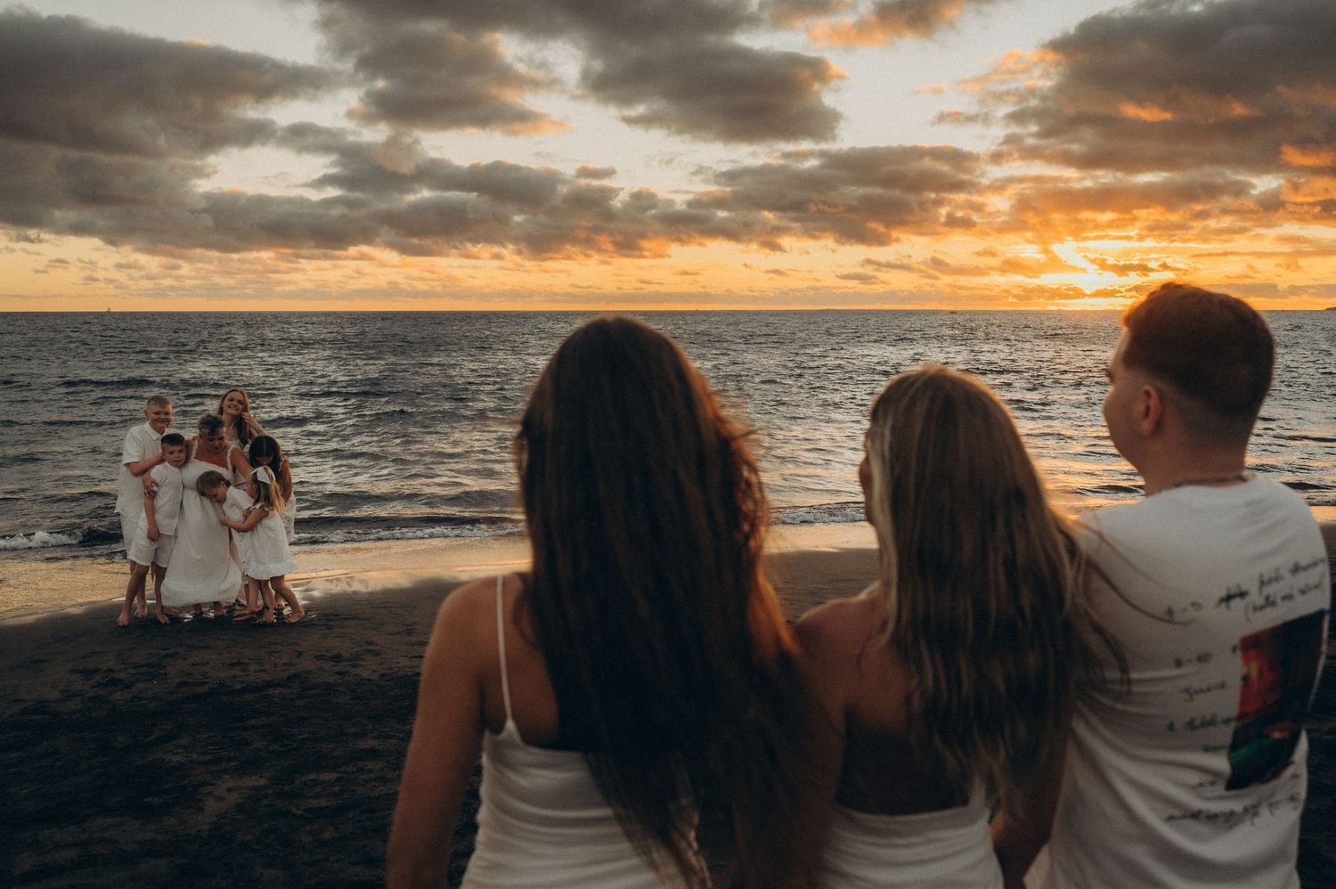 Large family photoshoot on Tenerife beach with silhouettes of people watching dramatic orange and purple sunset over the ocean