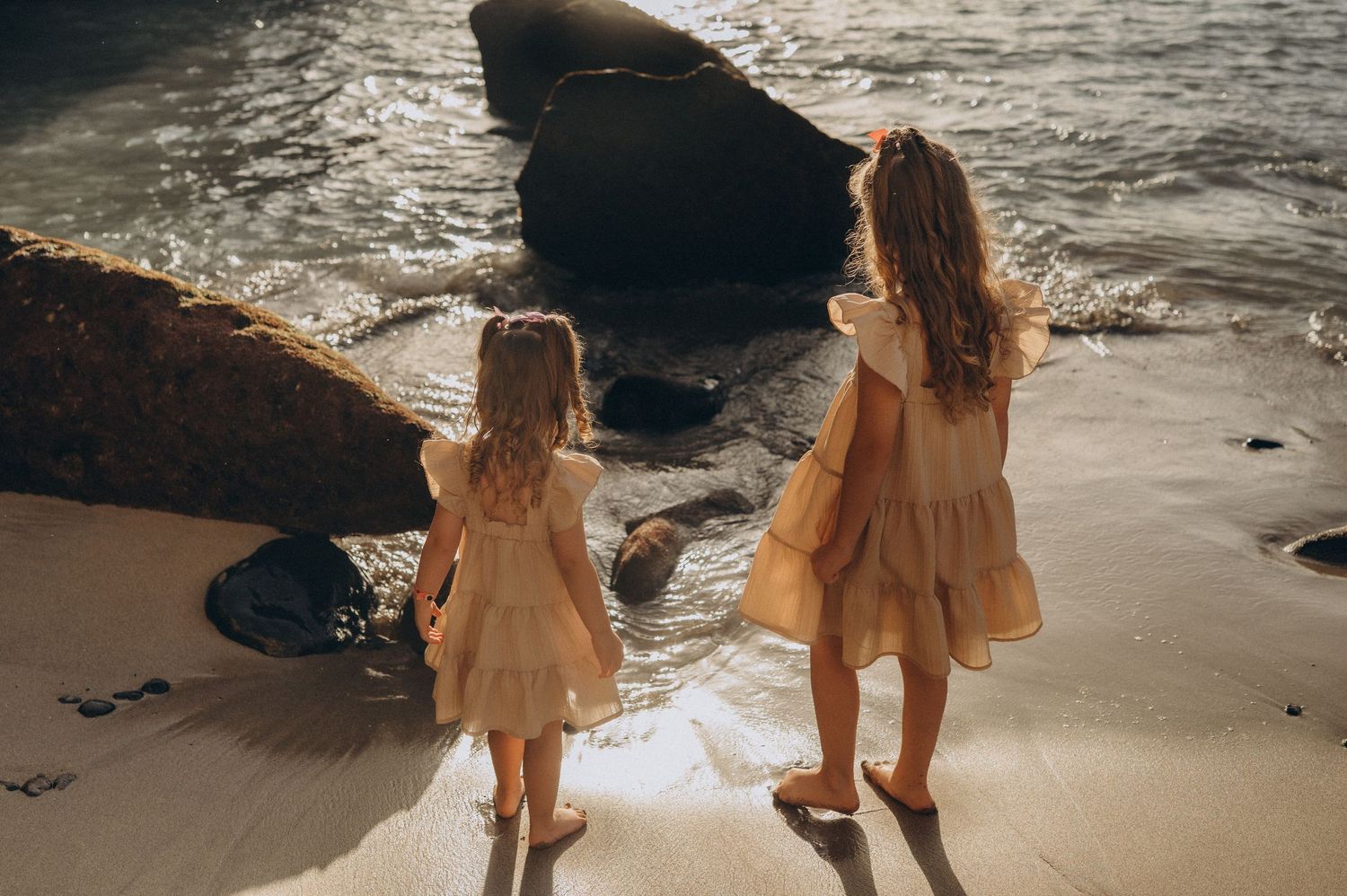 Two sisters side by side on white-golden sand with ocean waves during sunset session, Tenerife