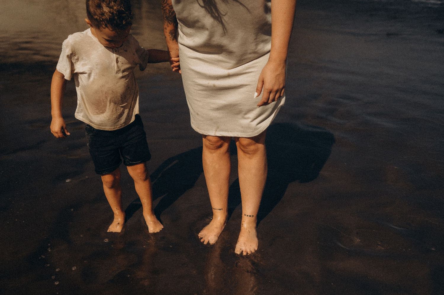 Close-up of family’s feet on dark sand beach, Playa del Duque Tenerife
