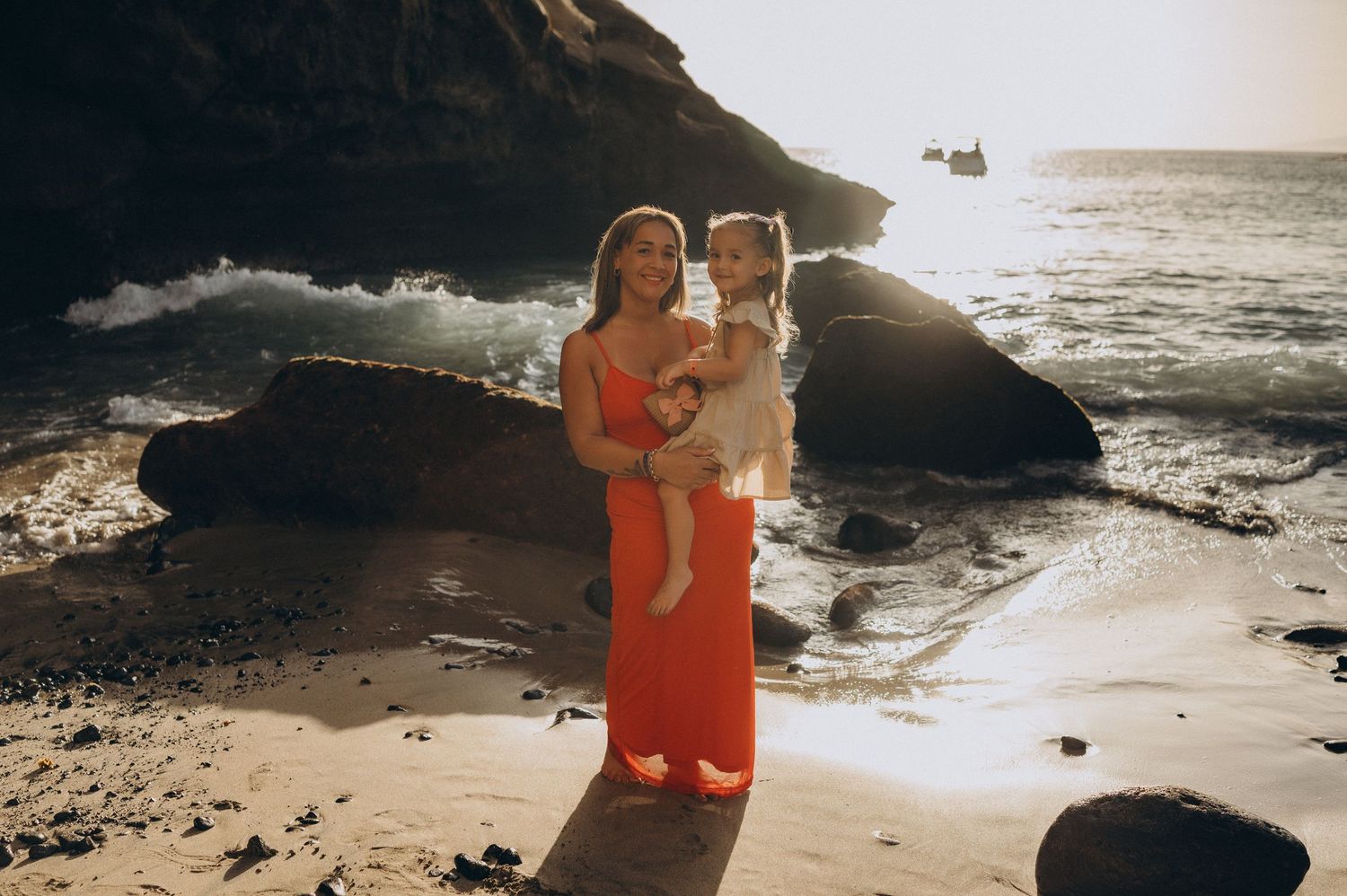 Tender moment of mother holding daughter with golden sunset and Atlantic waves at Playa Morteros