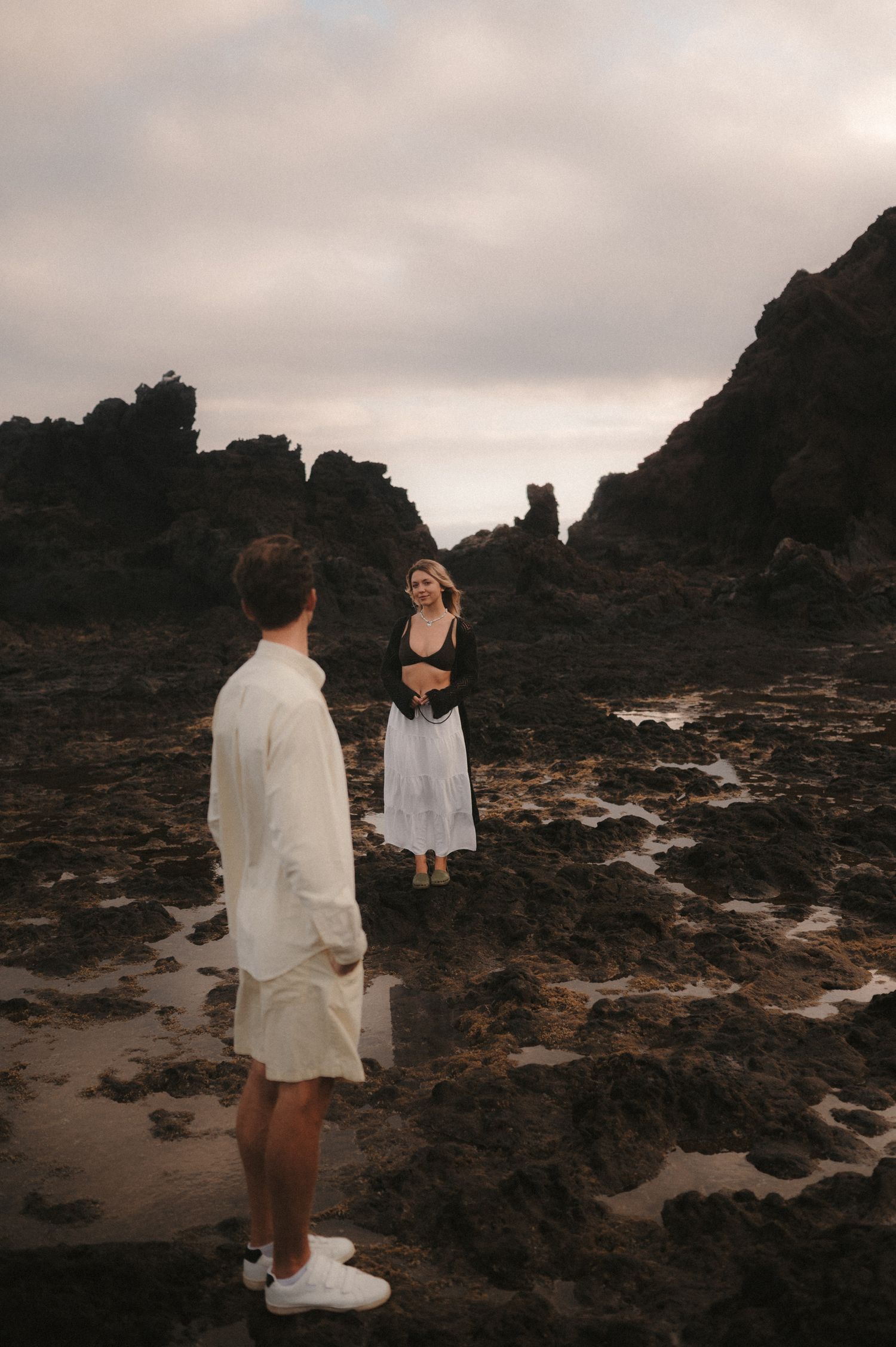 Loving couple standing face-to-face on rocks by the ocean during low tide, in a secluded spot under Montaña Roja, Tenerife