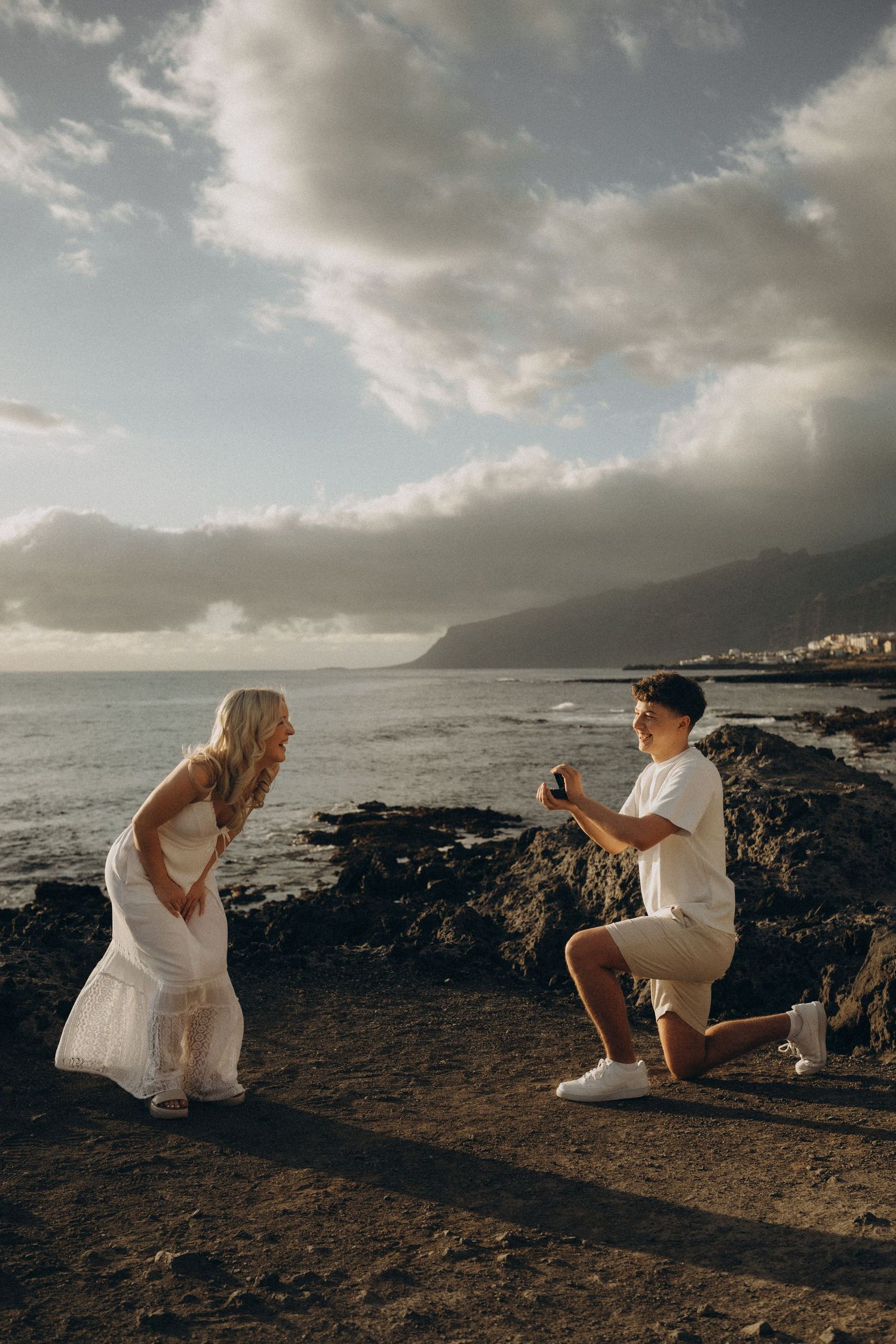 Surprise proposal in Los Gigantes, Tenerife on a rocky ocean shore at sunset with mountains in the background.