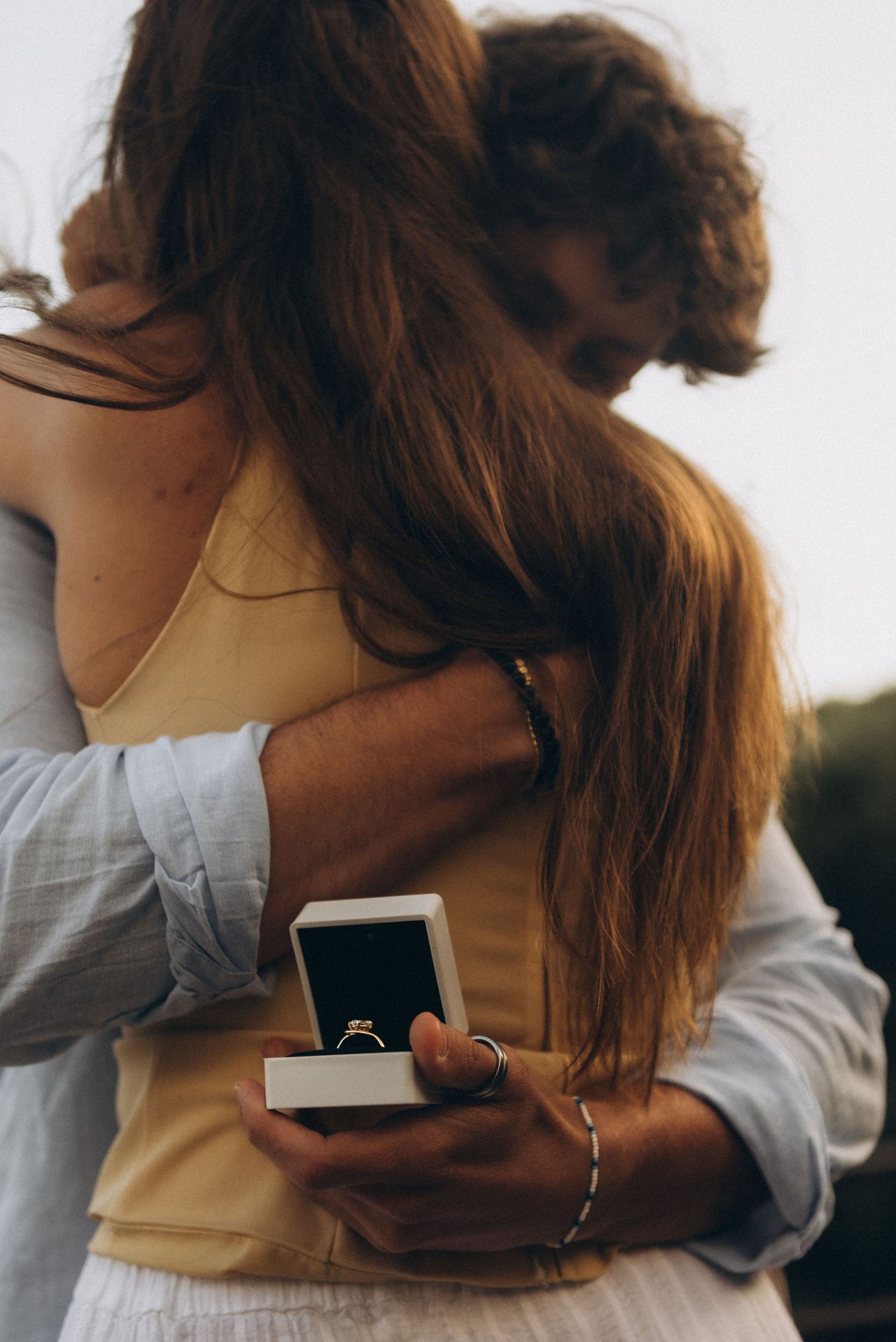 Couple embracing during a romantic marriage proposal, man holding an open ring box with a diamond engagement ring.