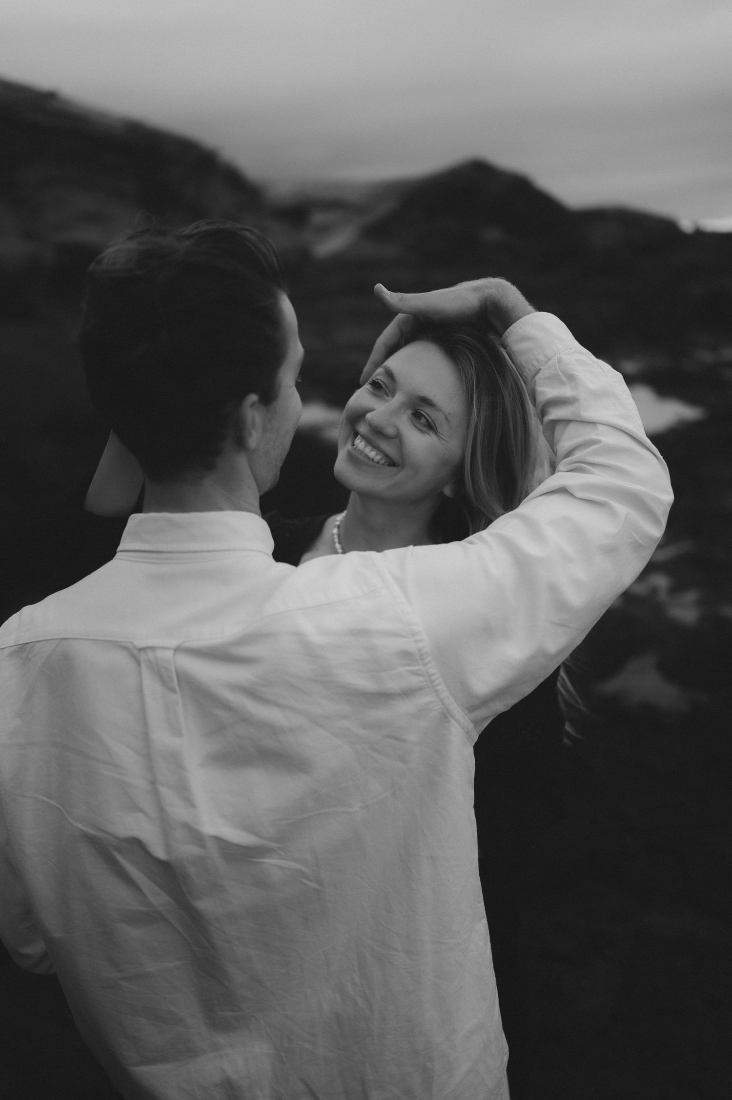 Young romantic couple during a photoshoot, touching each other’s hair, smiling and gazing into each other’s eyes, sharing a loving moment in