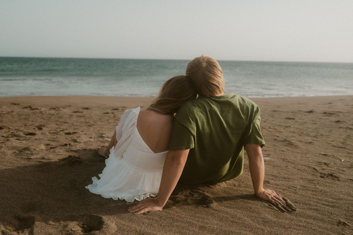 Young couple sitting side by side on Playa Tejita, she rests her head on his shoulder while they gaze at the ocean, Tenerife couples photosh