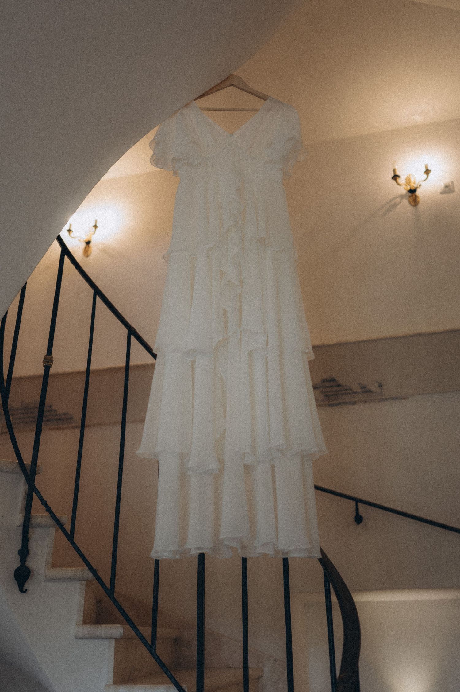 Bridal wedding dress hanging in an elegant entrance hall with a vintage castle-style staircase in the background.