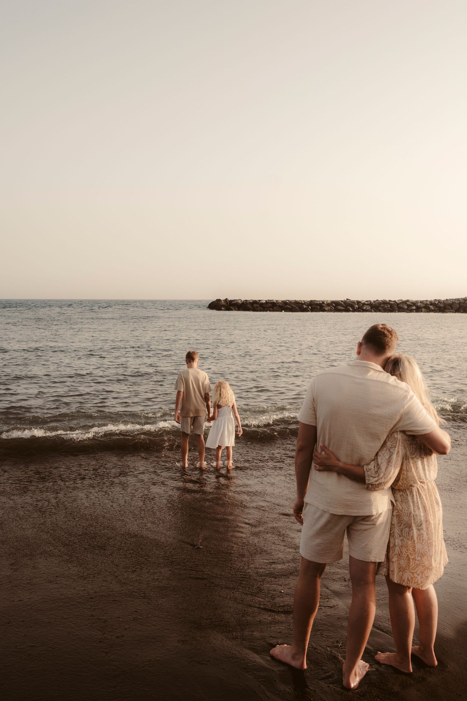 Parents watching their beloved children play by ocean at sunset, Playa del Duque