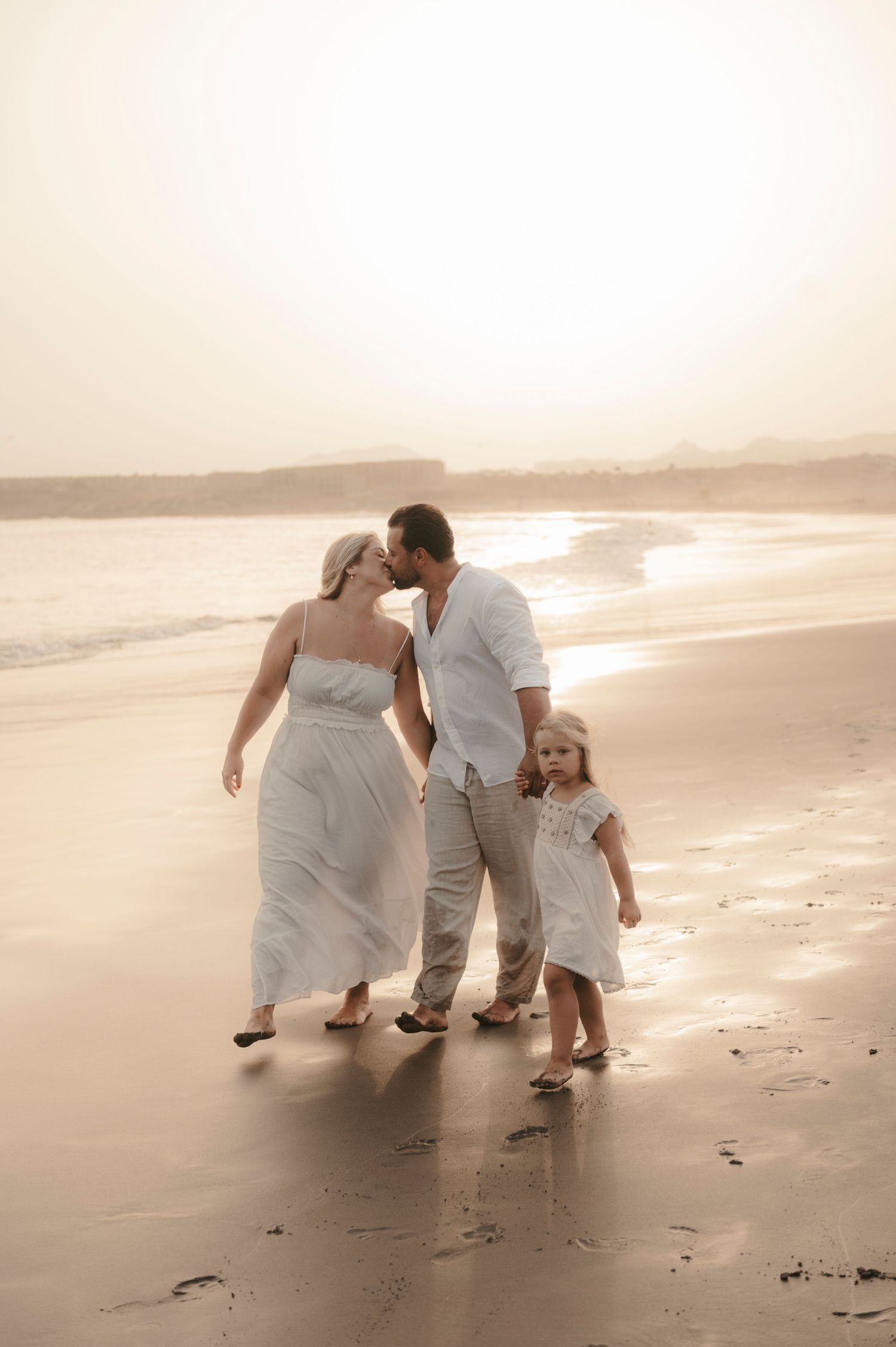 Tender moment of parents and daughter embracing while watching the colorful sunset by the ocean at Playa La Tejita