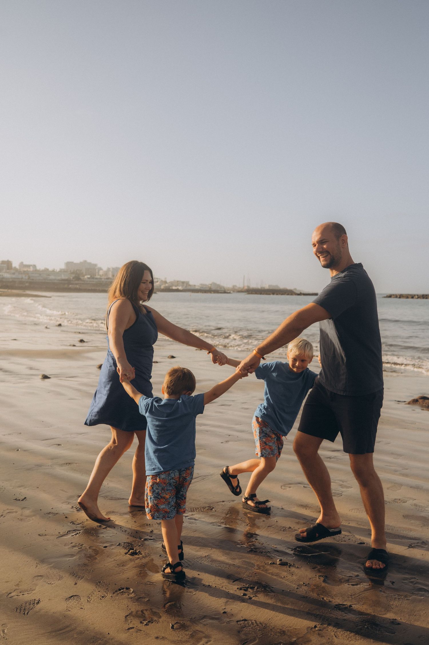Tender scene of family laughing and twirling together in a circle by the ocean at Playa Fañabé