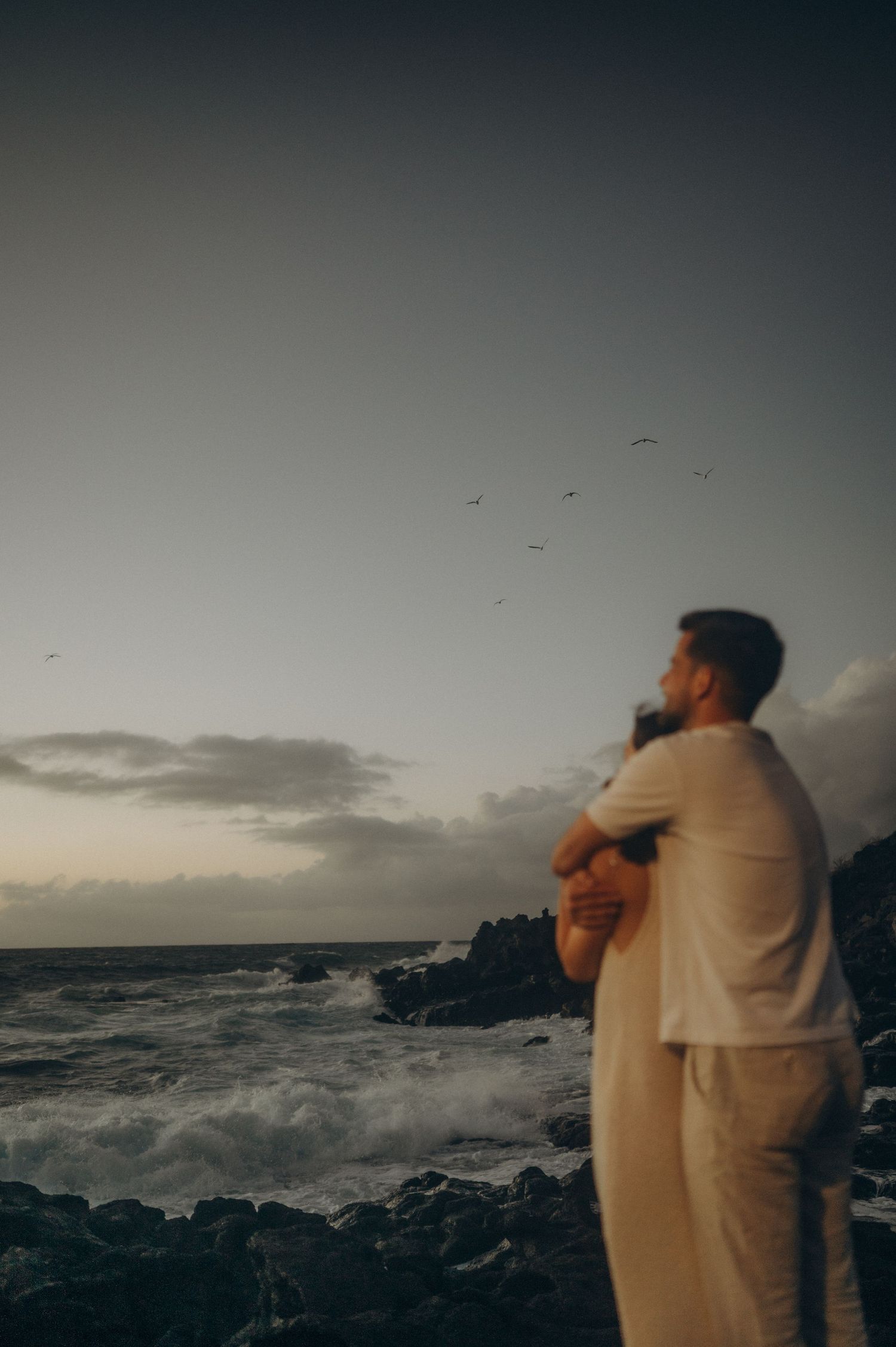 Man hugging fiancée after engagement on Tenerife volcanic cliffs beach