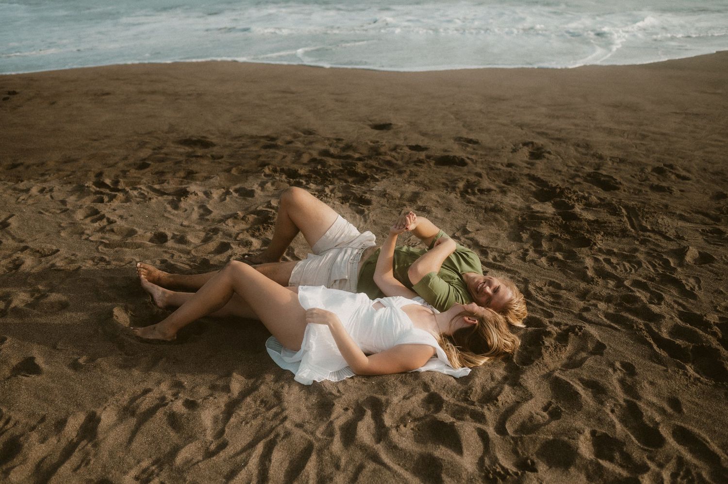 Young couple lying side by side on the warm summer sand at Playa Tejita, laughing together, Tenerife couples photoshoot