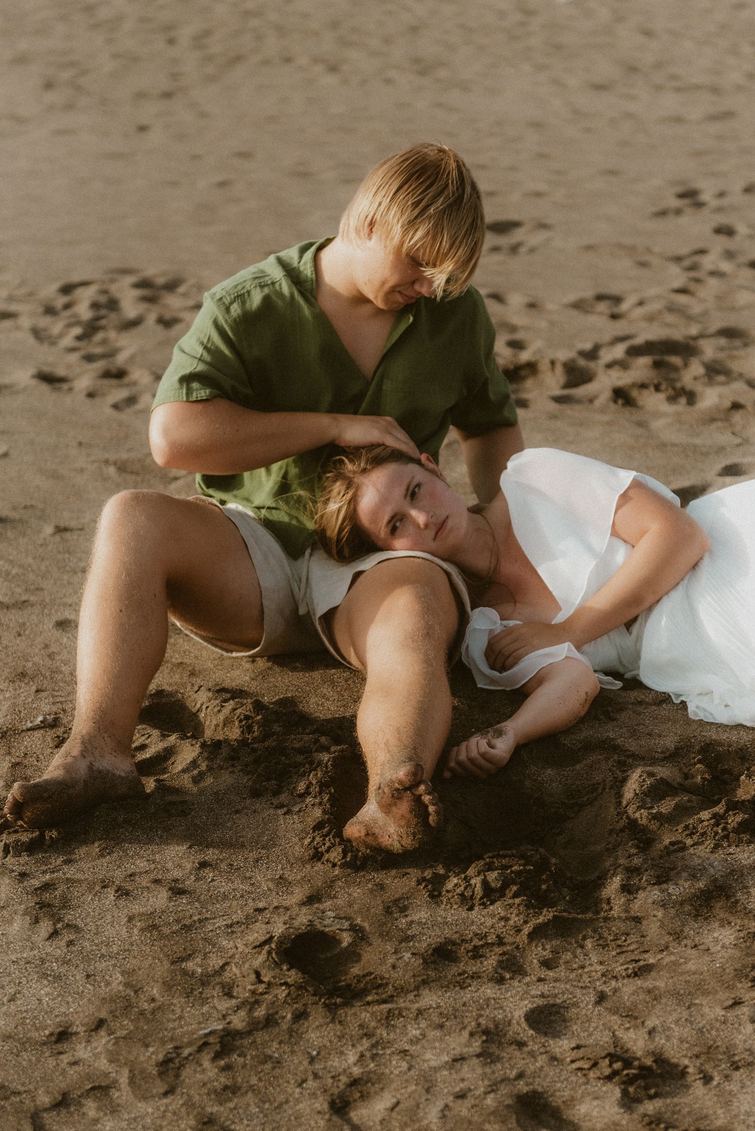 Woman lying on her partner's lap while he gently strokes her hair, enjoying the warm sand on Playa Tejita, Tenerife couples photoshoot