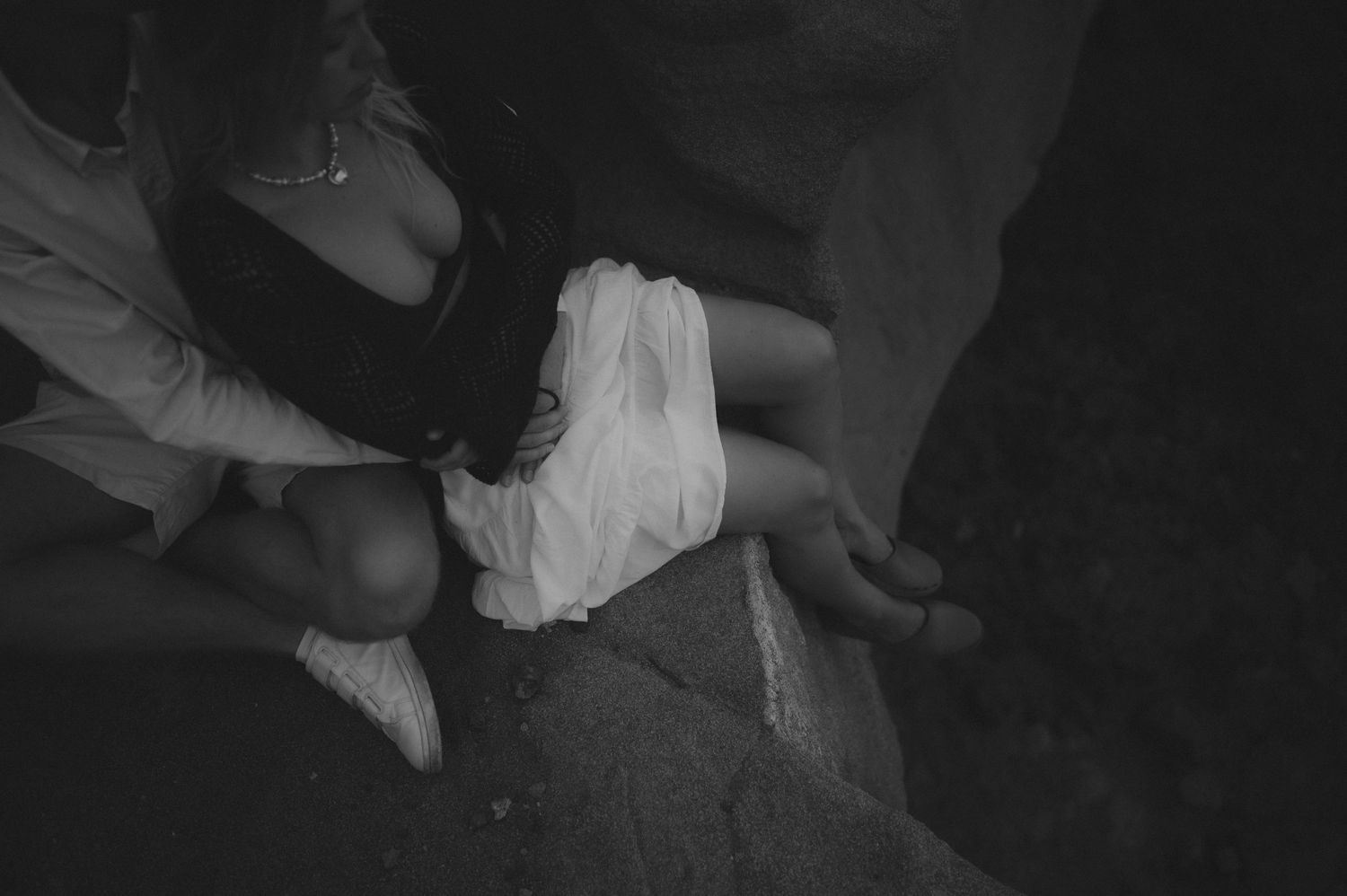 Young romantic couple sitting on a cliff with their legs dangling in the wind, enjoying a photoshoot in Tenerife
