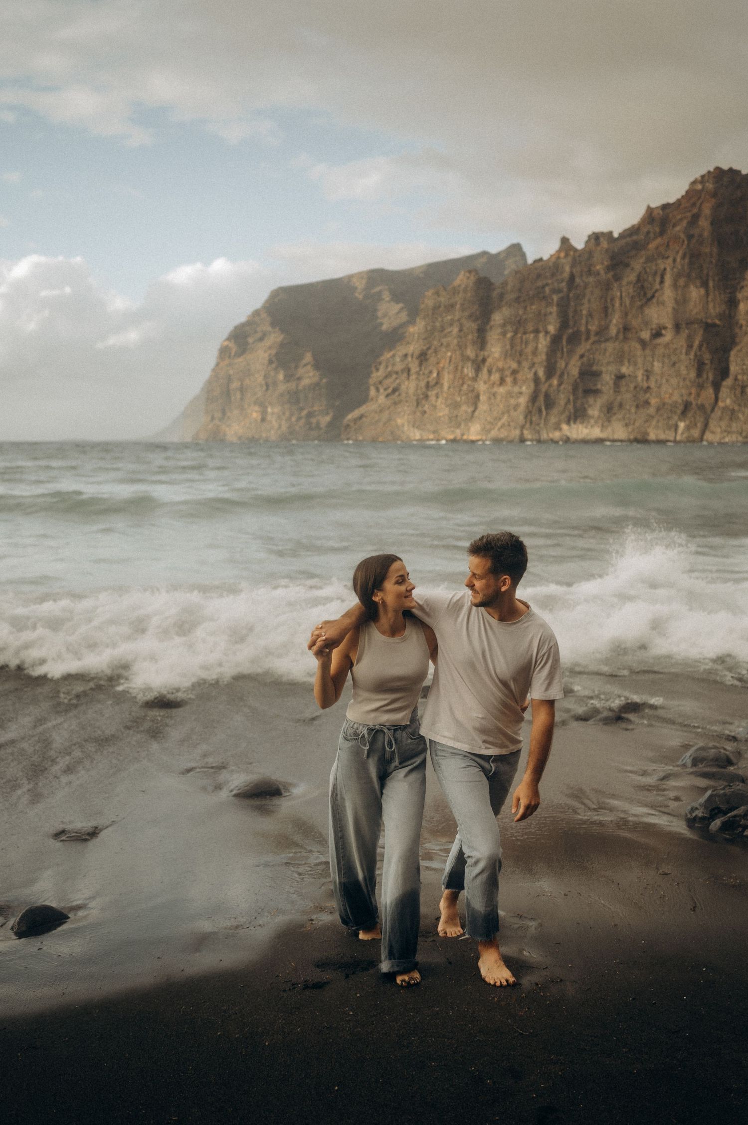Romantic couple strolling on Playa de Los Guíos with ocean and cliffs in the background, Tenerife