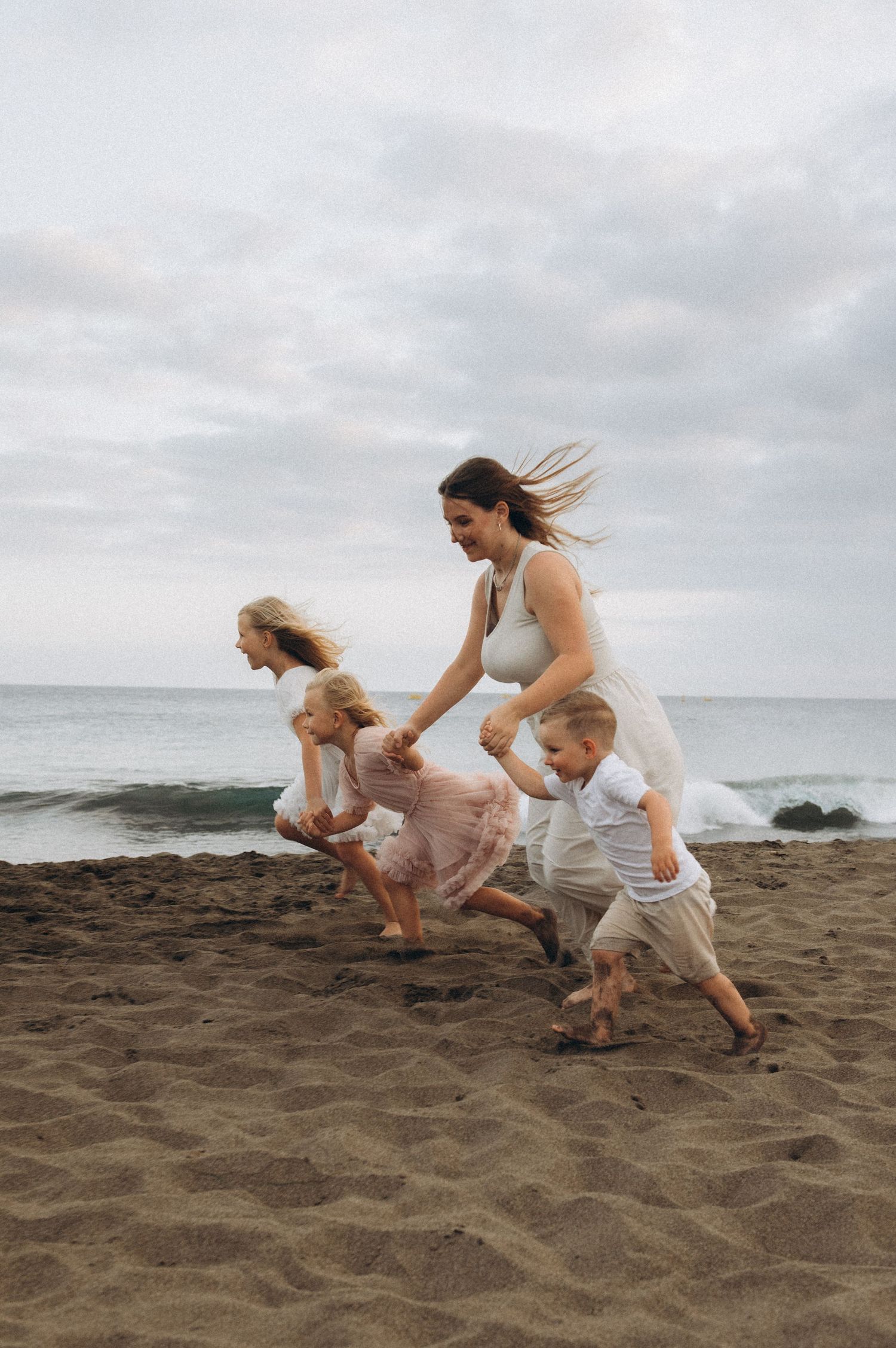 Family running on Playa La Tejita, oldest sister holding hands with young children, Tenerife