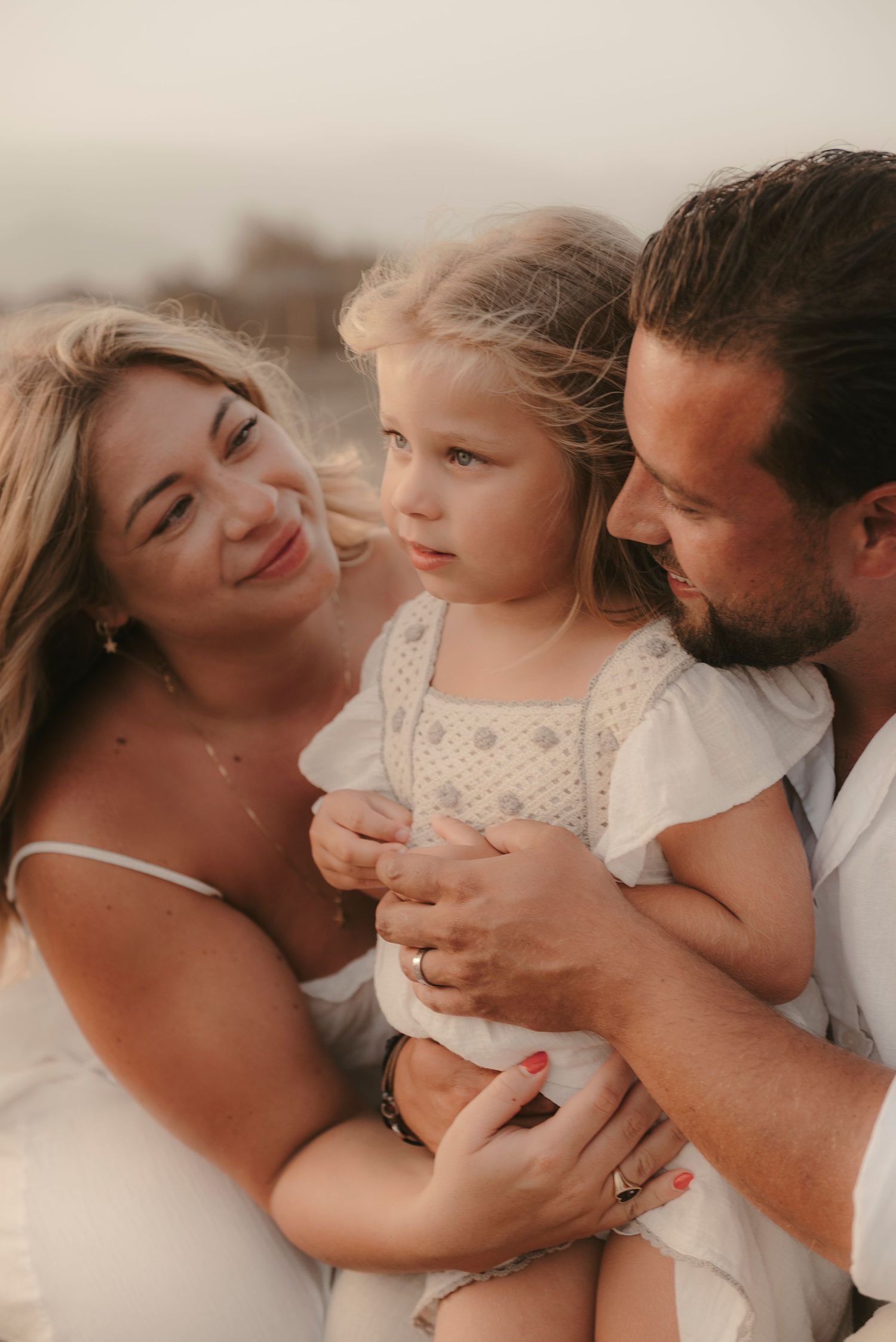 Close-up of parents crouching and hugging their daughter in the center