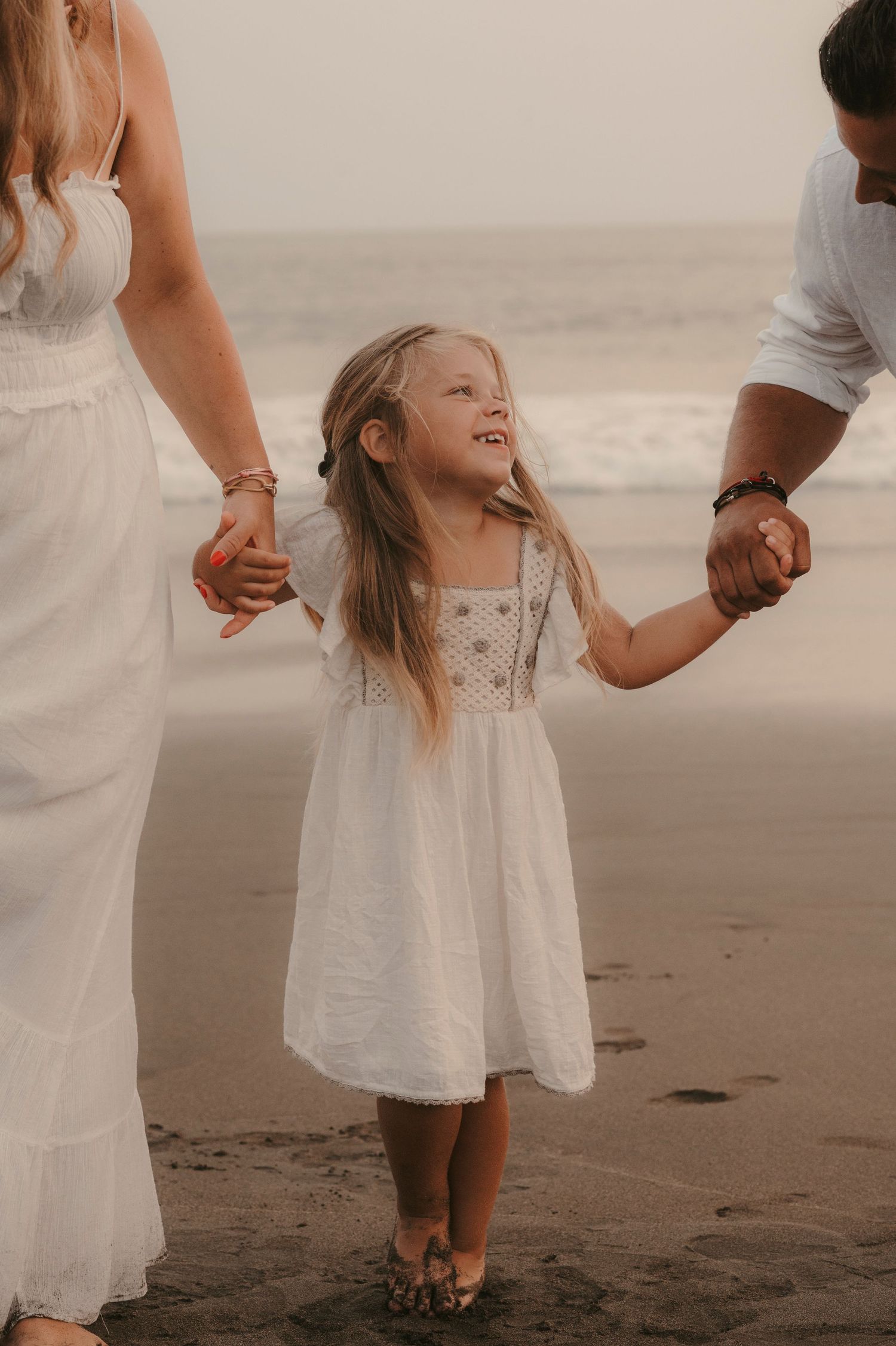 Joyful family moment with little girl smiling at her dad while walking hand in hand at Playa La Tejita