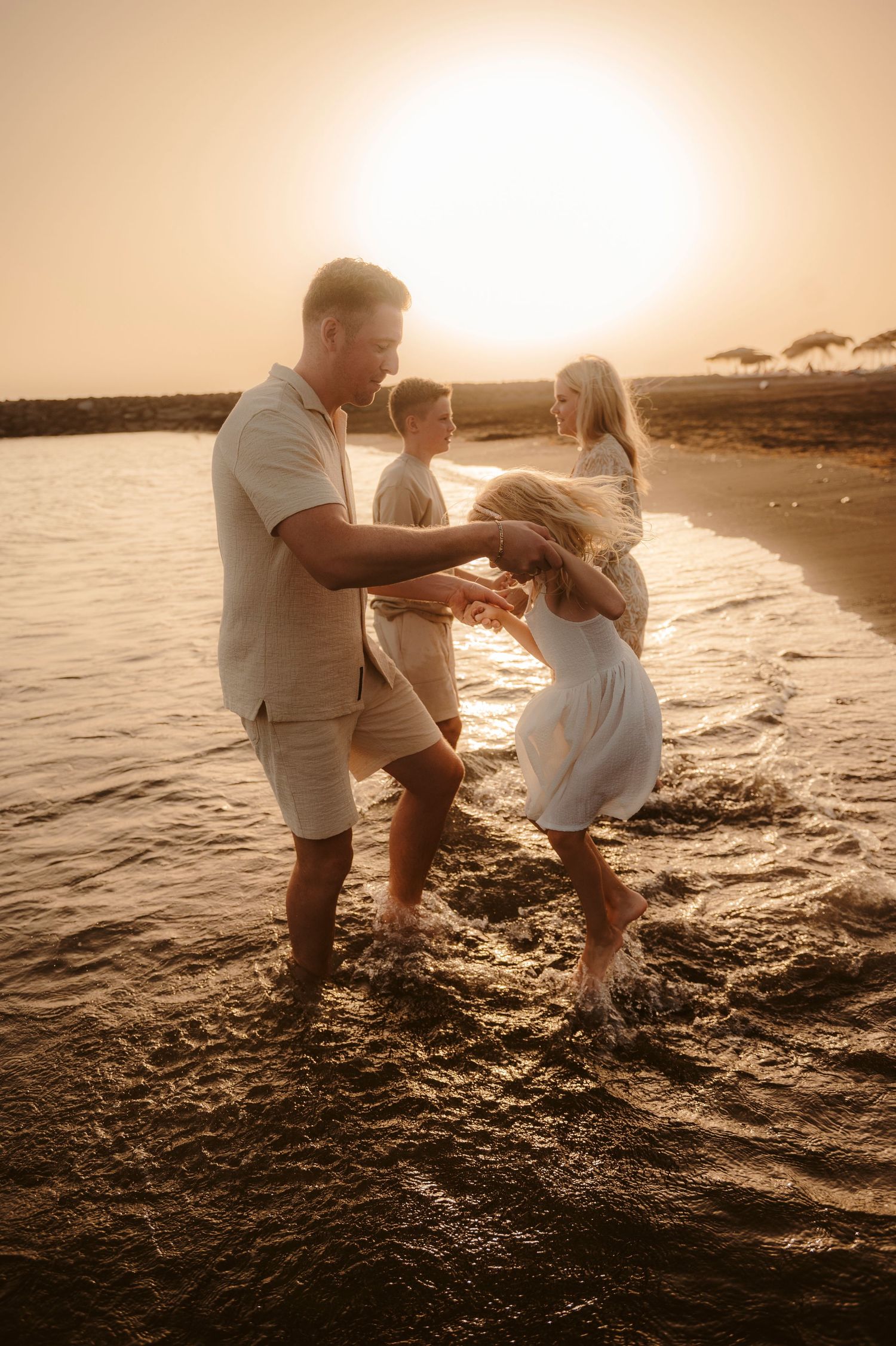 Family holding hands standing in water with sunset in background.