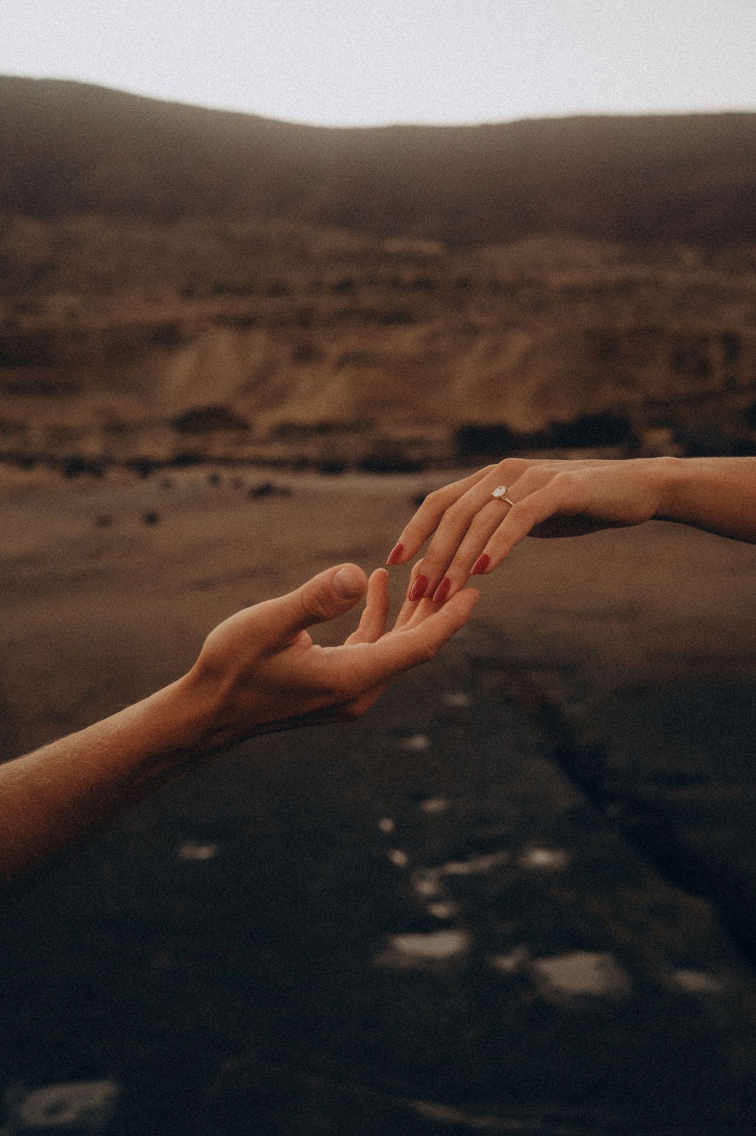 Close-up of a woman gently touching her partner's open hand, showcasing her engagement ring during a couple photoshoot in Tenerife.