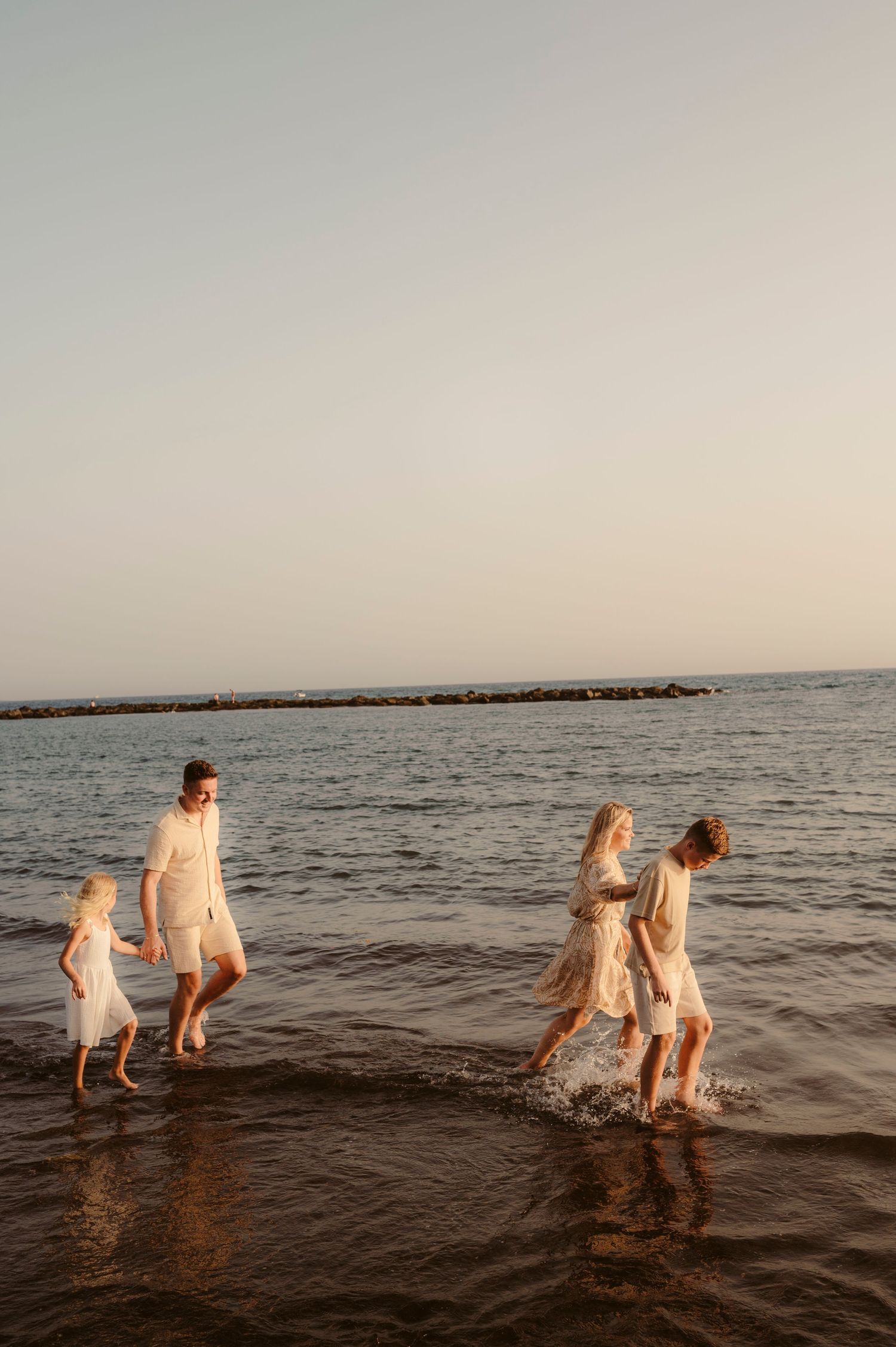 Family moment with parents looking at children playing on beach at sunset, Playa del Duque