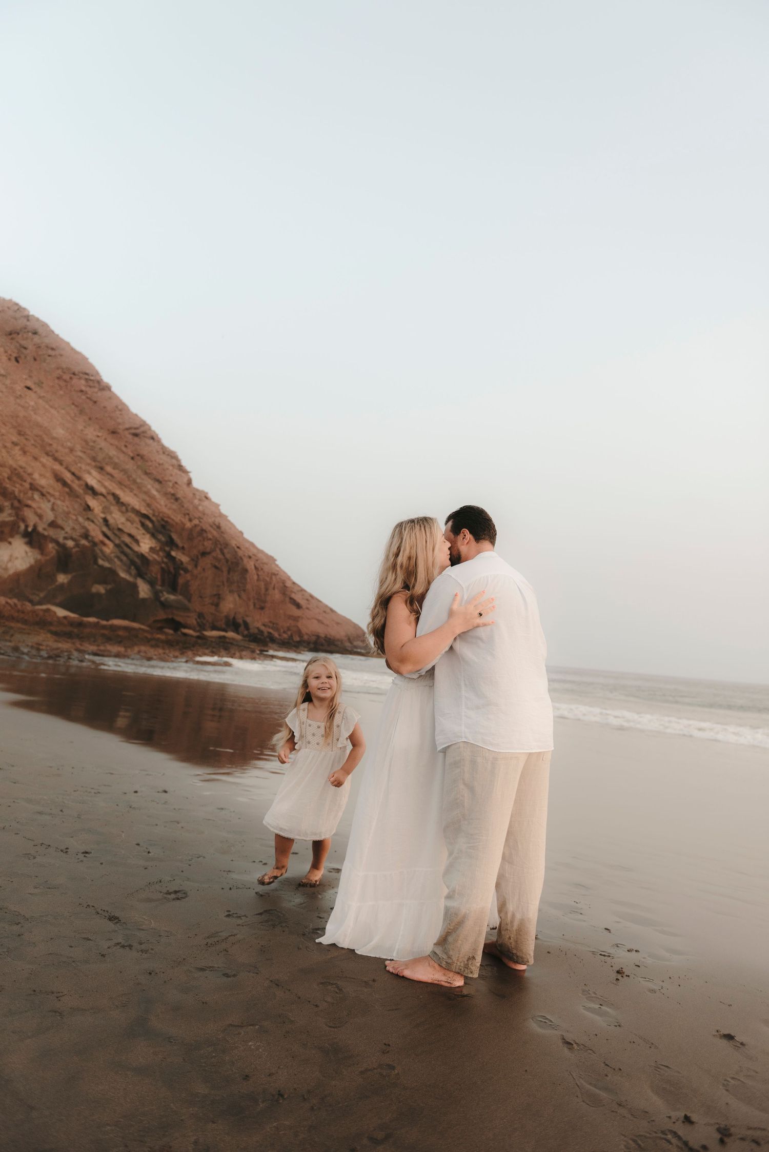 Warm family interaction with father and mother close and daughter playing by the shore with Montaña Roja volcano in view at Playa La Tejita