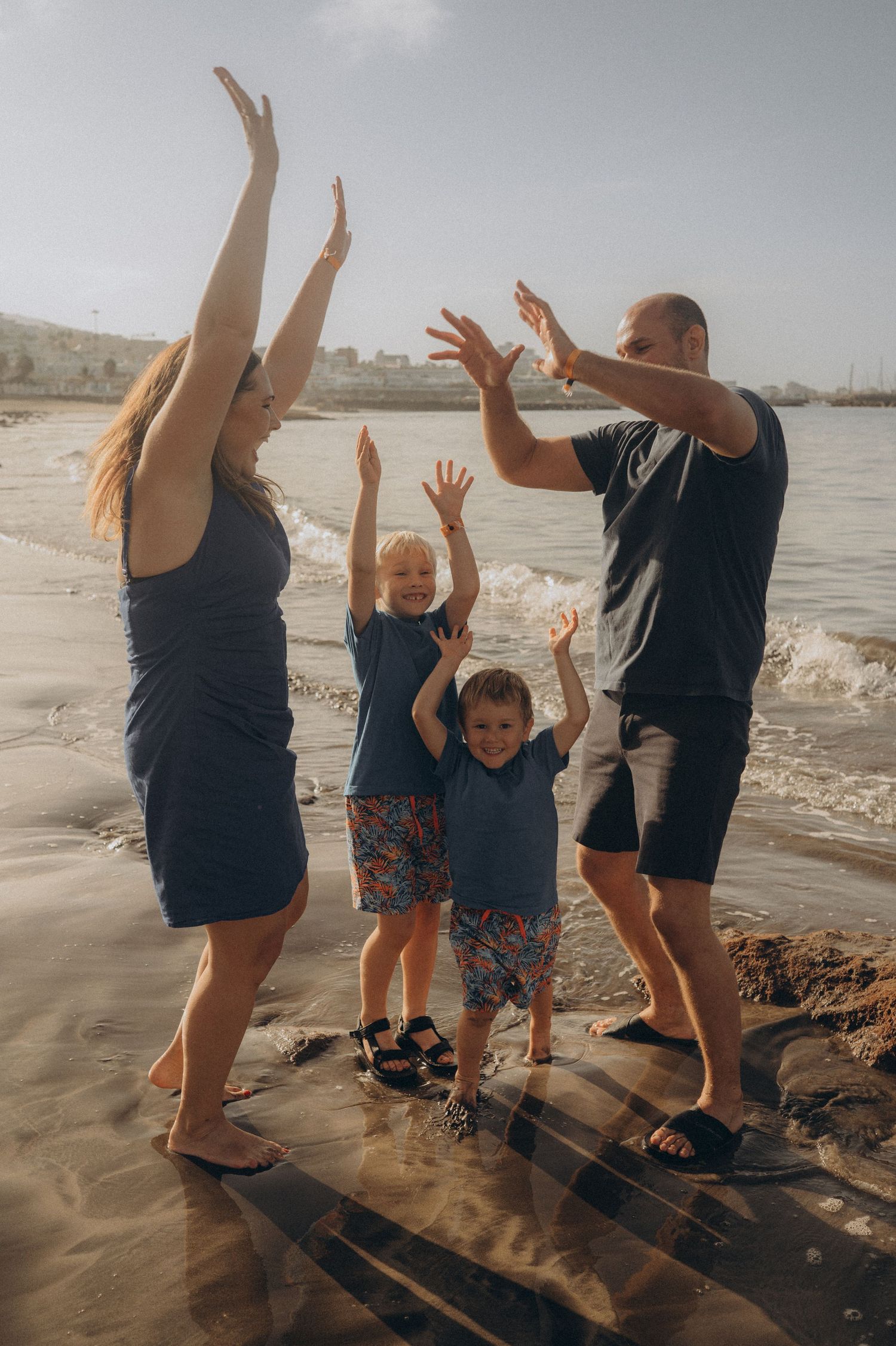 Family of four laughing with raised hands by the ocean at Playa Fañabé during morning session