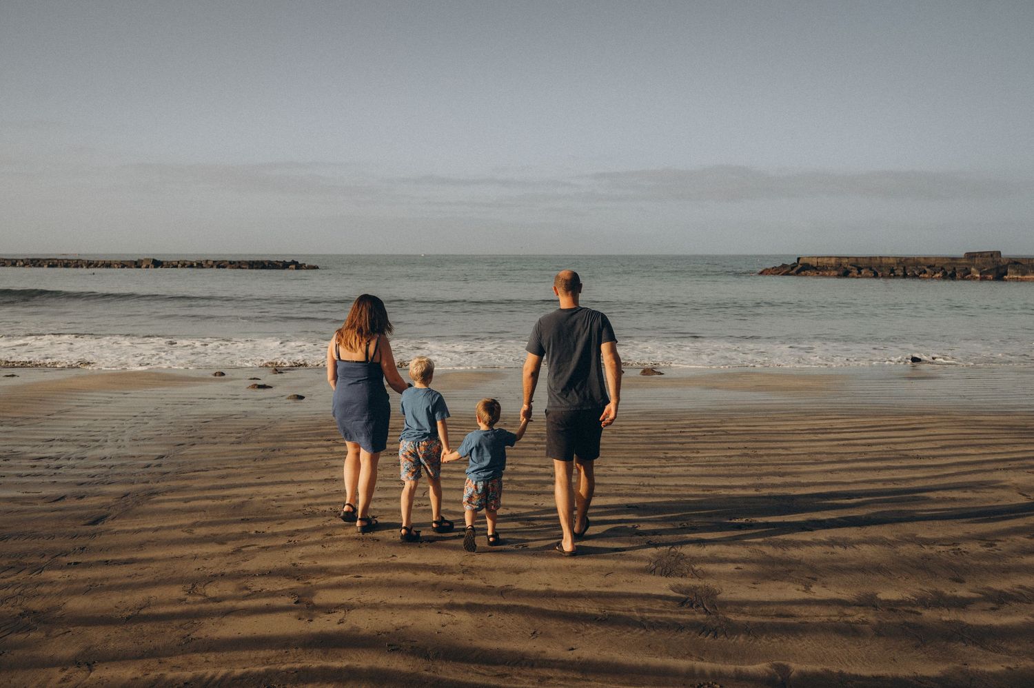 Parents and children strolling hand in hand toward the Atlantic Ocean on Playa Fañabé beach during sunrise