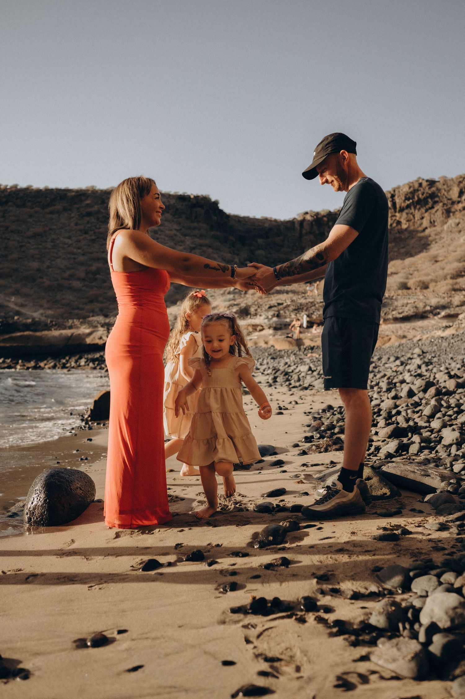 Happy family playing with kids on a Tenerife beach by the ocean at golden sunset