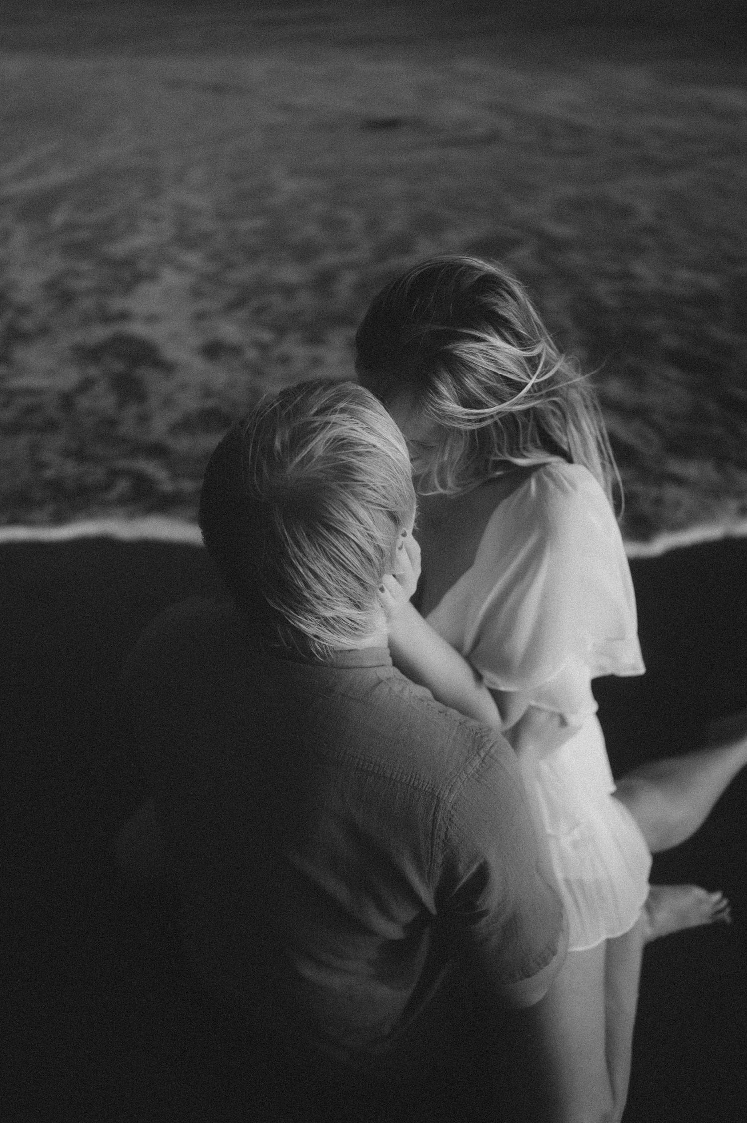 Young couple cuddling in the shallow ocean waves at Playa Tejita, sunset and waves creating a romantic scene, Tenerife couples photoshoot