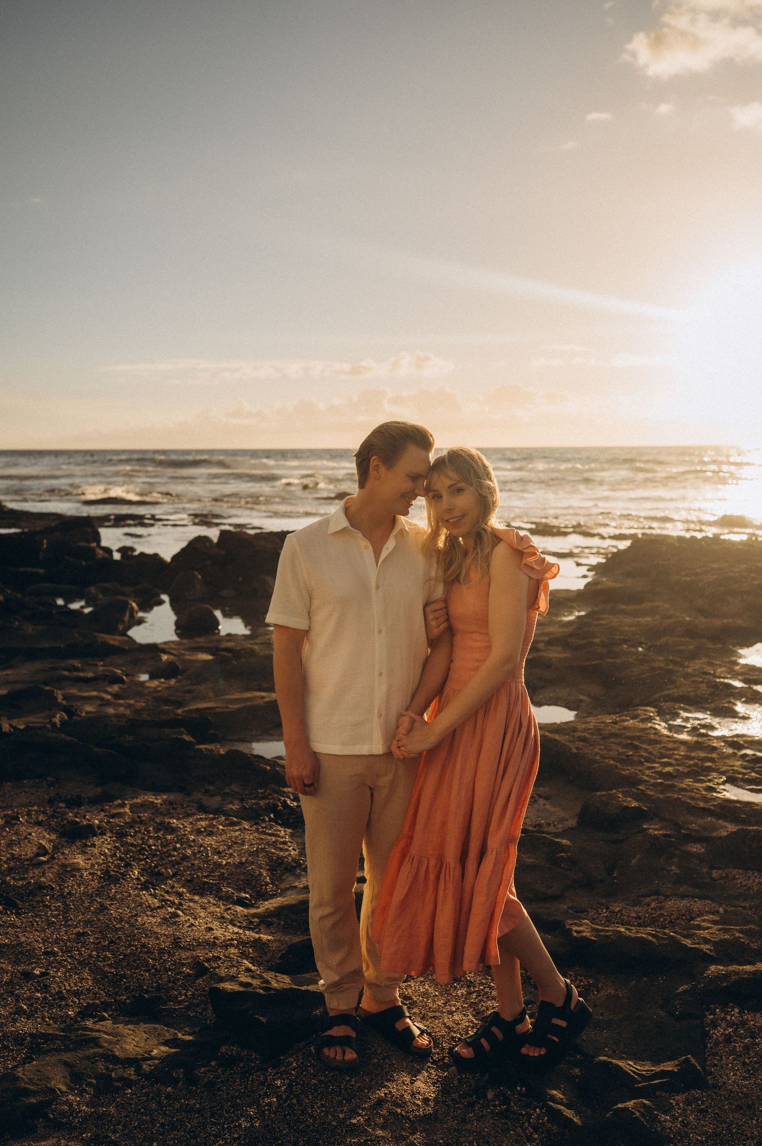 Couple at sunset, side by side with him holding her in arms, ocean behind, Las Americas