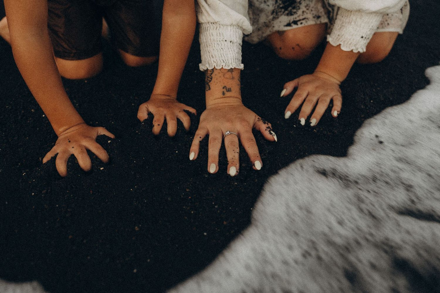 Close-up of mom and son hands touching and exploring textured sand on Tenerife beach during family photoshoot.