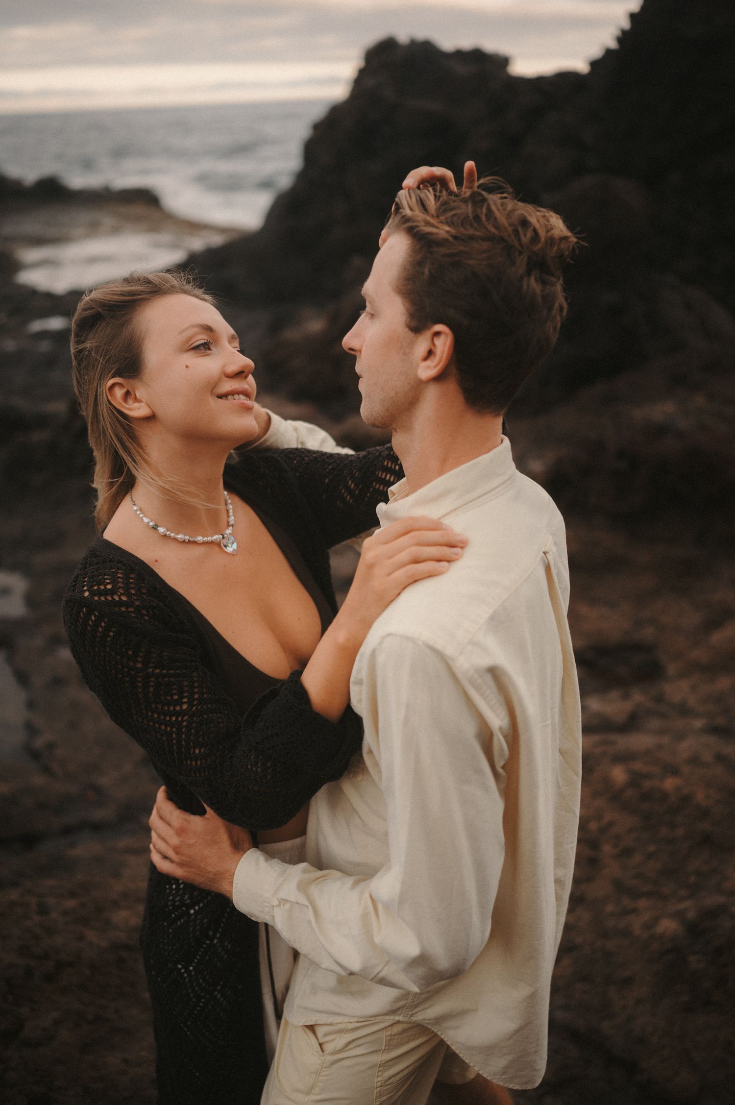 Close-up of a young couple looking into each other’s eyes, romantic moment with ocean and cliffs in the background, Tenerife