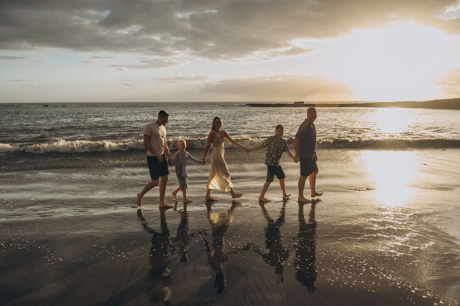 Parents and children strolling on sand holding hands with sunset behind, Playa Fañabé
