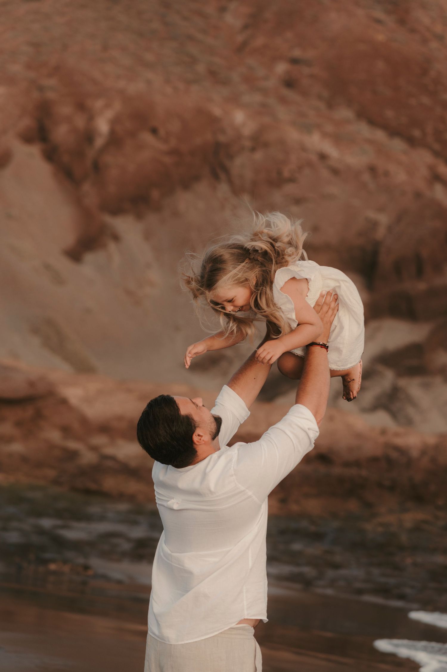 Energetic family scene of father tossing his daughter in the air with big smiles at Playa La Tejita