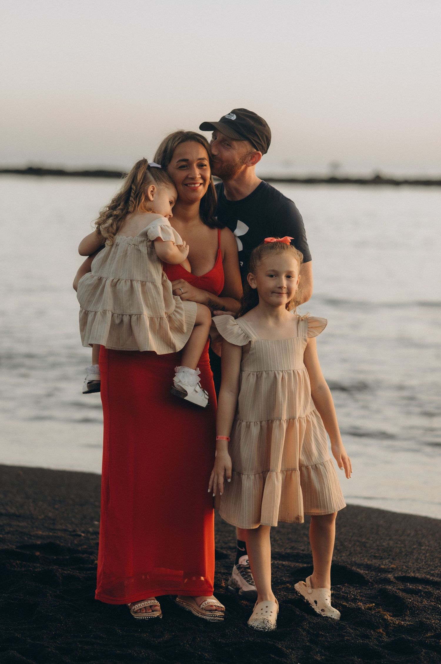 Father hugging his family from behind on a black sand beach during sunset in Tenerife