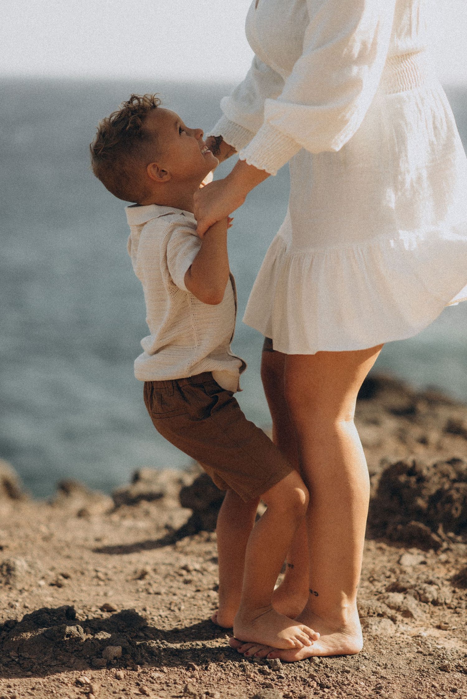 Mother holding toddler’s hands as he stands, gazing into each other’s eyes, Montaña Roja