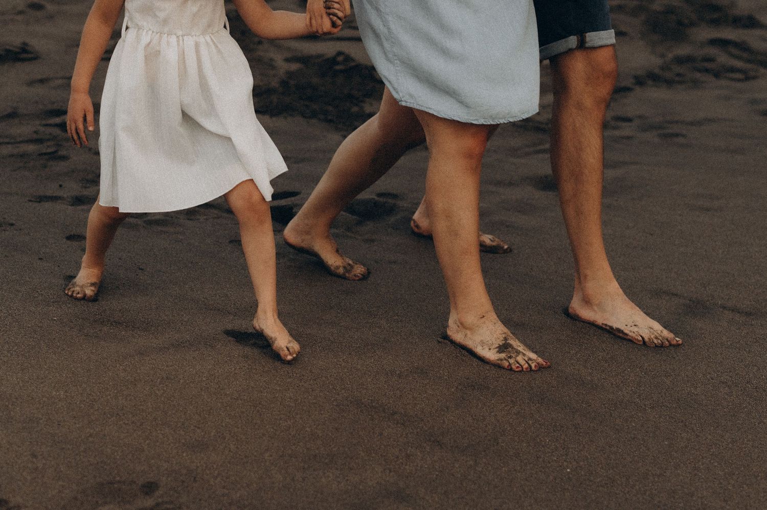 Bare feet of people walking in a line on dark sand at the beach Playa de La Tejita, Tenerife.