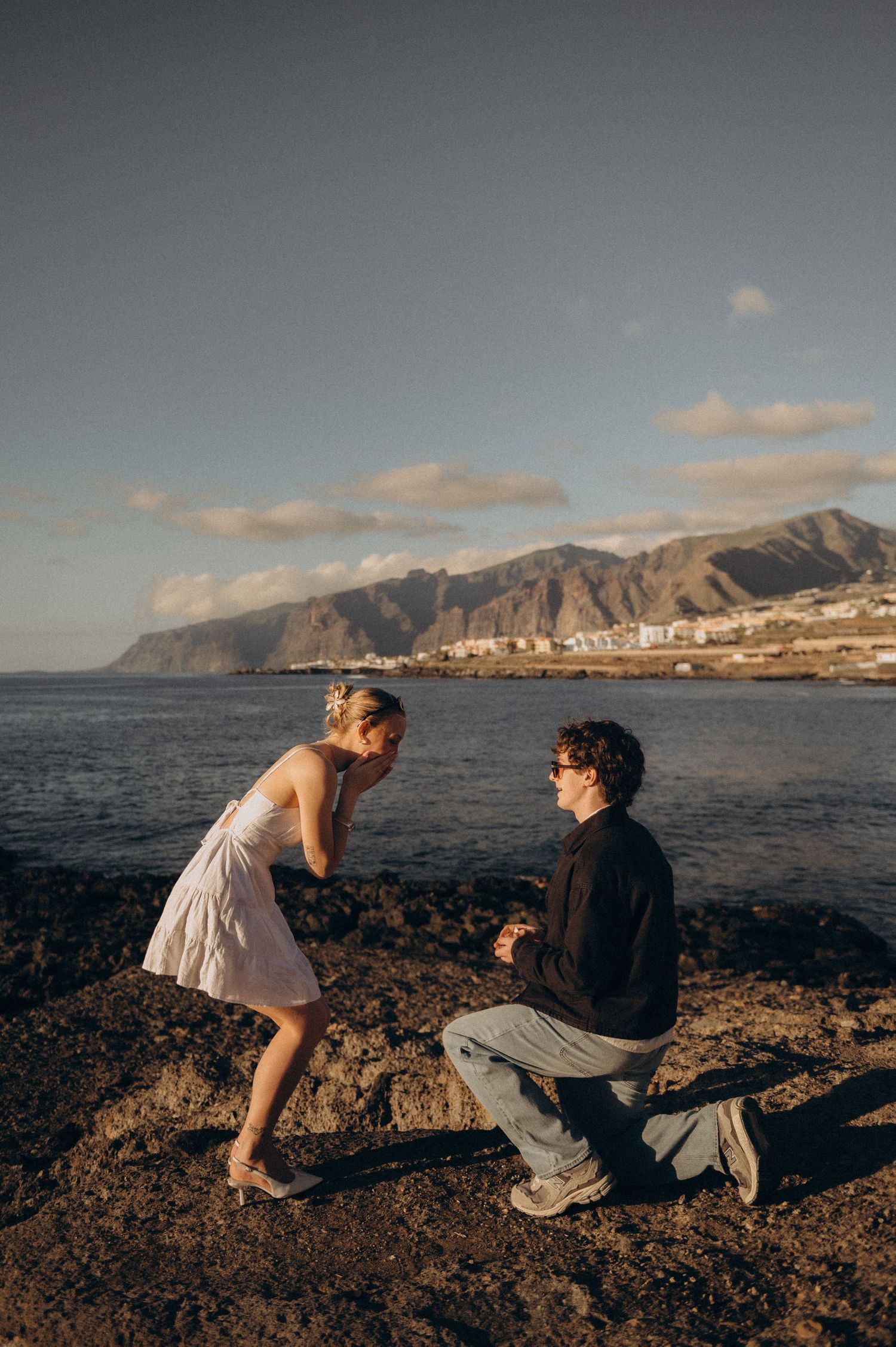 Surprise proposal in Los Gigantes, Tenerife on a rocky coastal shore with mountains and ocean at golden hour.