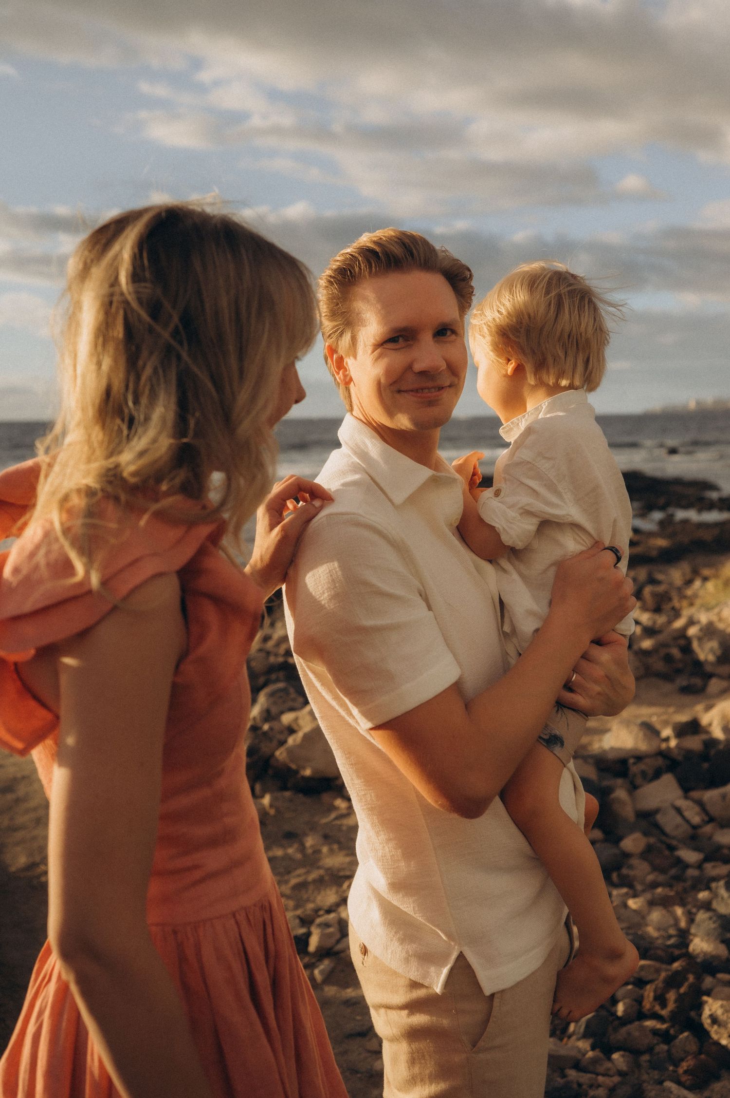 Father holding toddler while mother smiles at them by ocean, Las Americas Tenerife