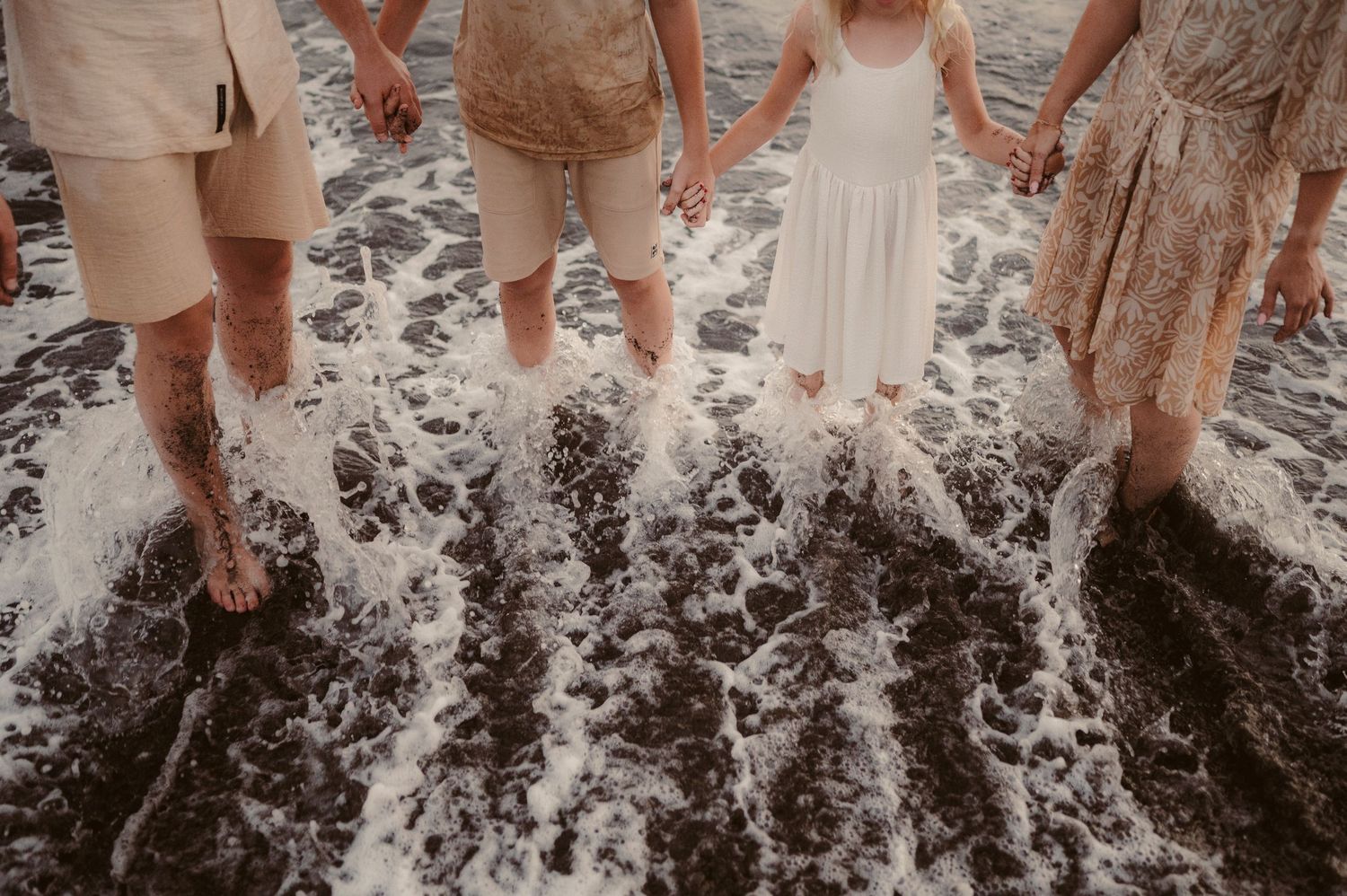 Children and parents holding hands in water at sunset