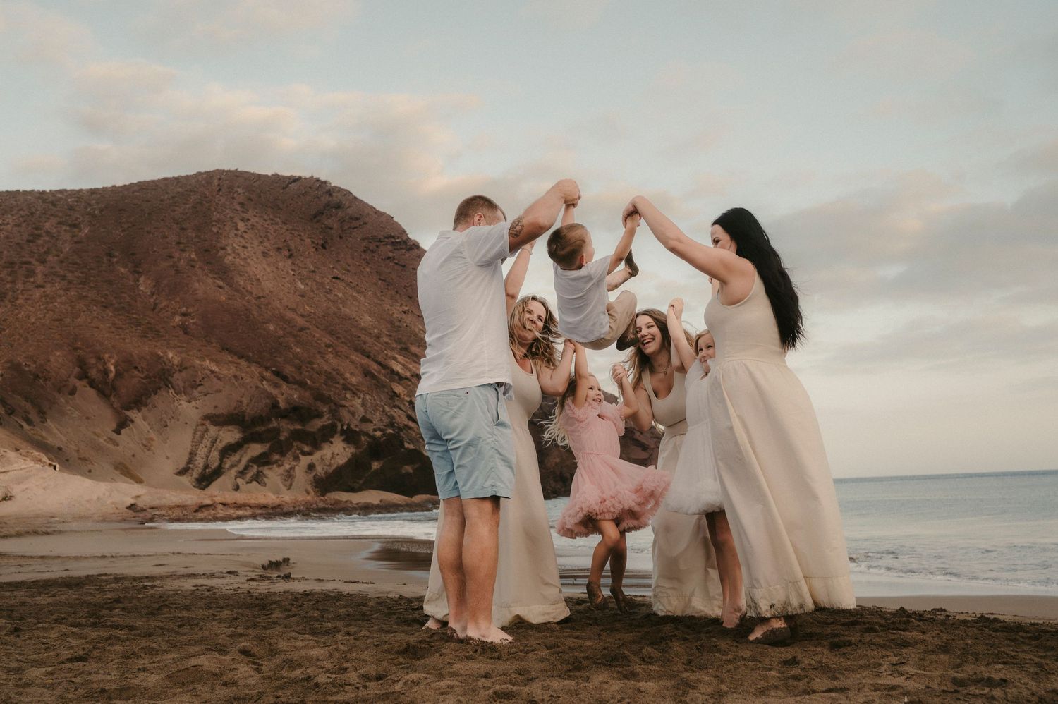 Large family at Playa La Tejita throwing youngest member in the air with Montana Roja behind