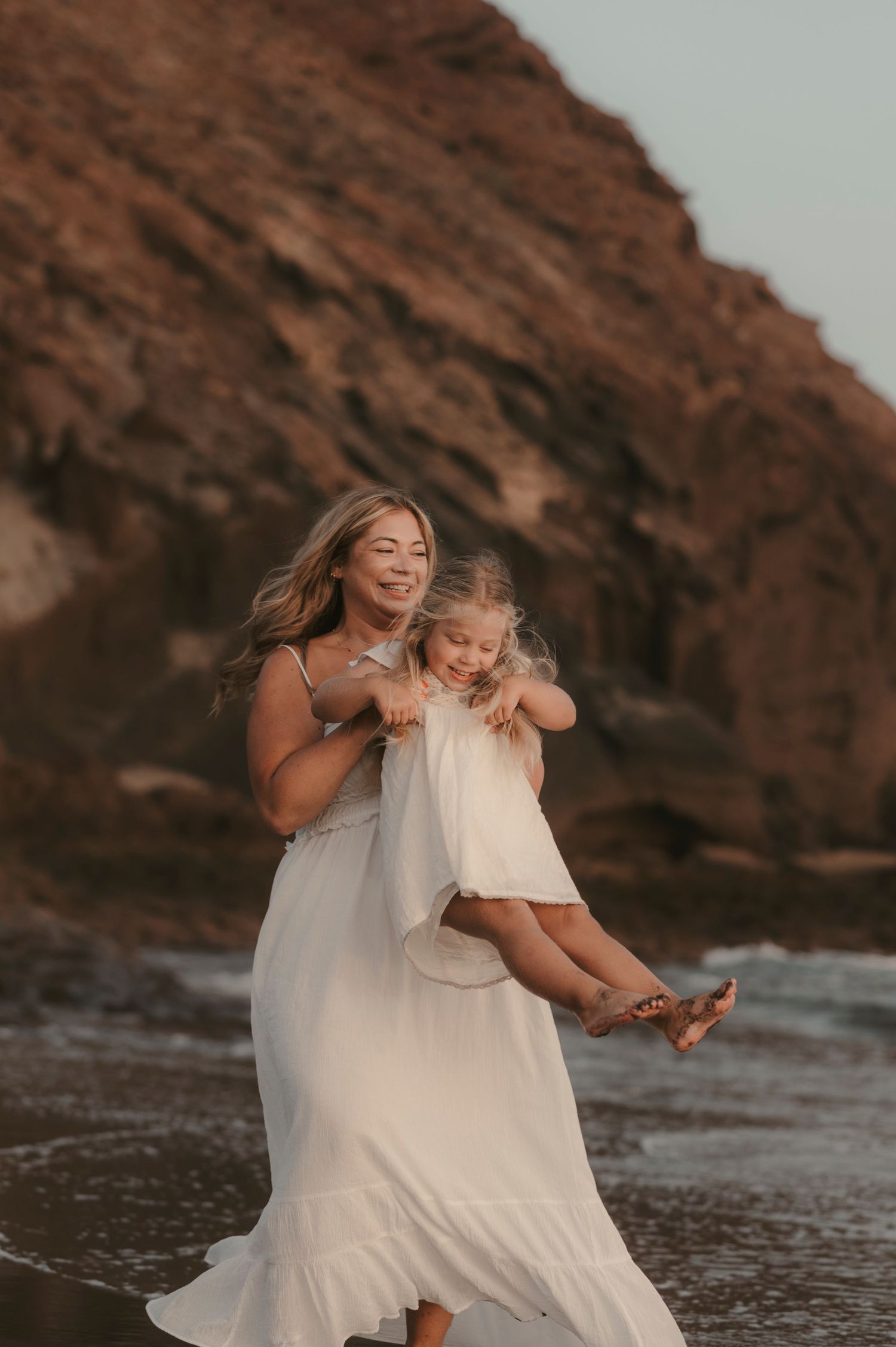 Magical moment of mother and daughter spinning together with big smiles near Montaña Roja and the Atlantic Ocean at Playa La Tejita