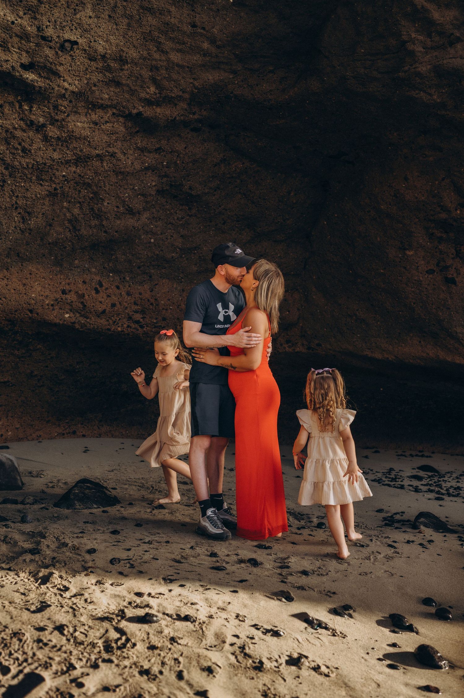 Children playing around parents beneath a rocky cave on a Tenerife coastline