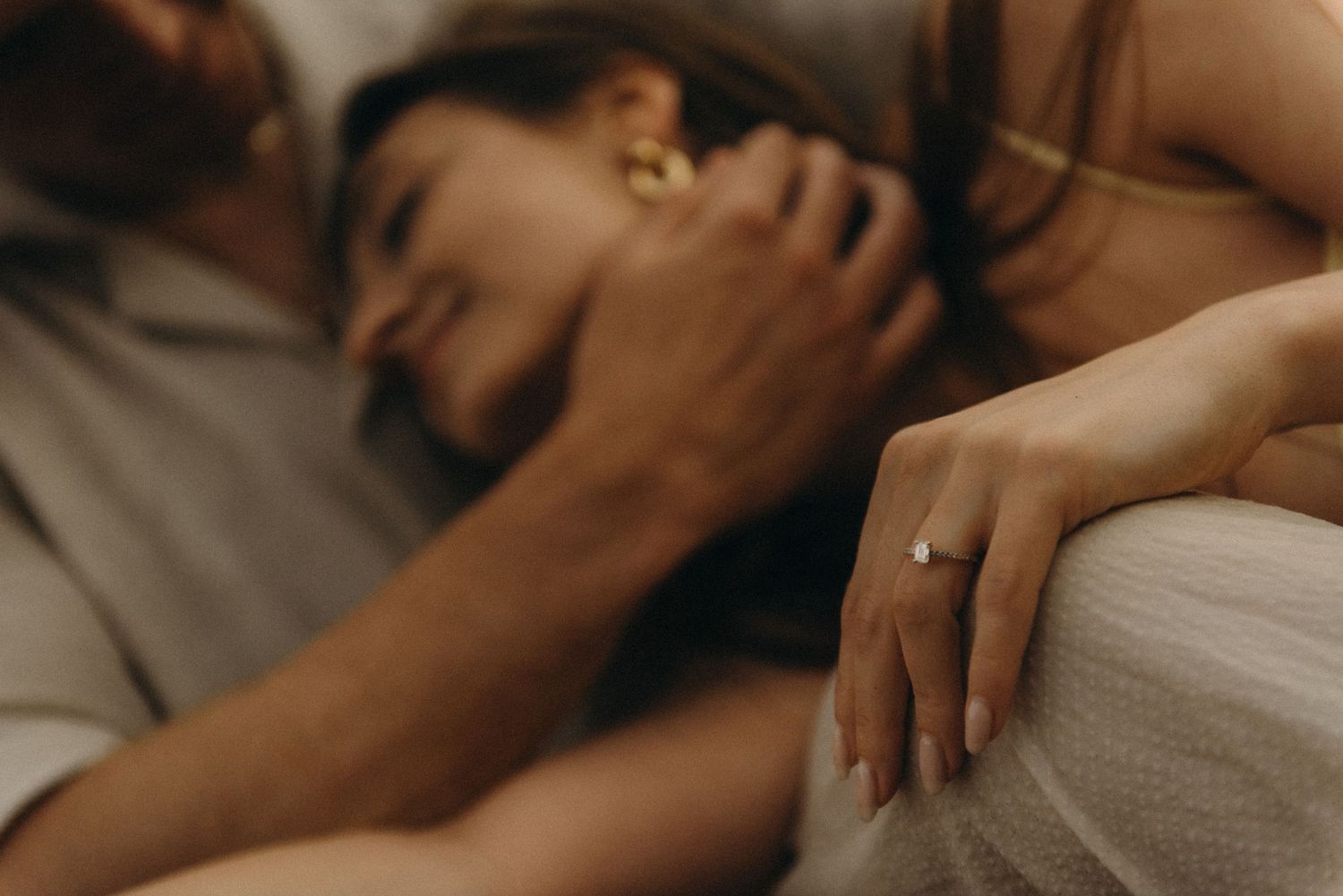 Couple lying close together, woman displaying elegant diamond engagement ring on her finger.