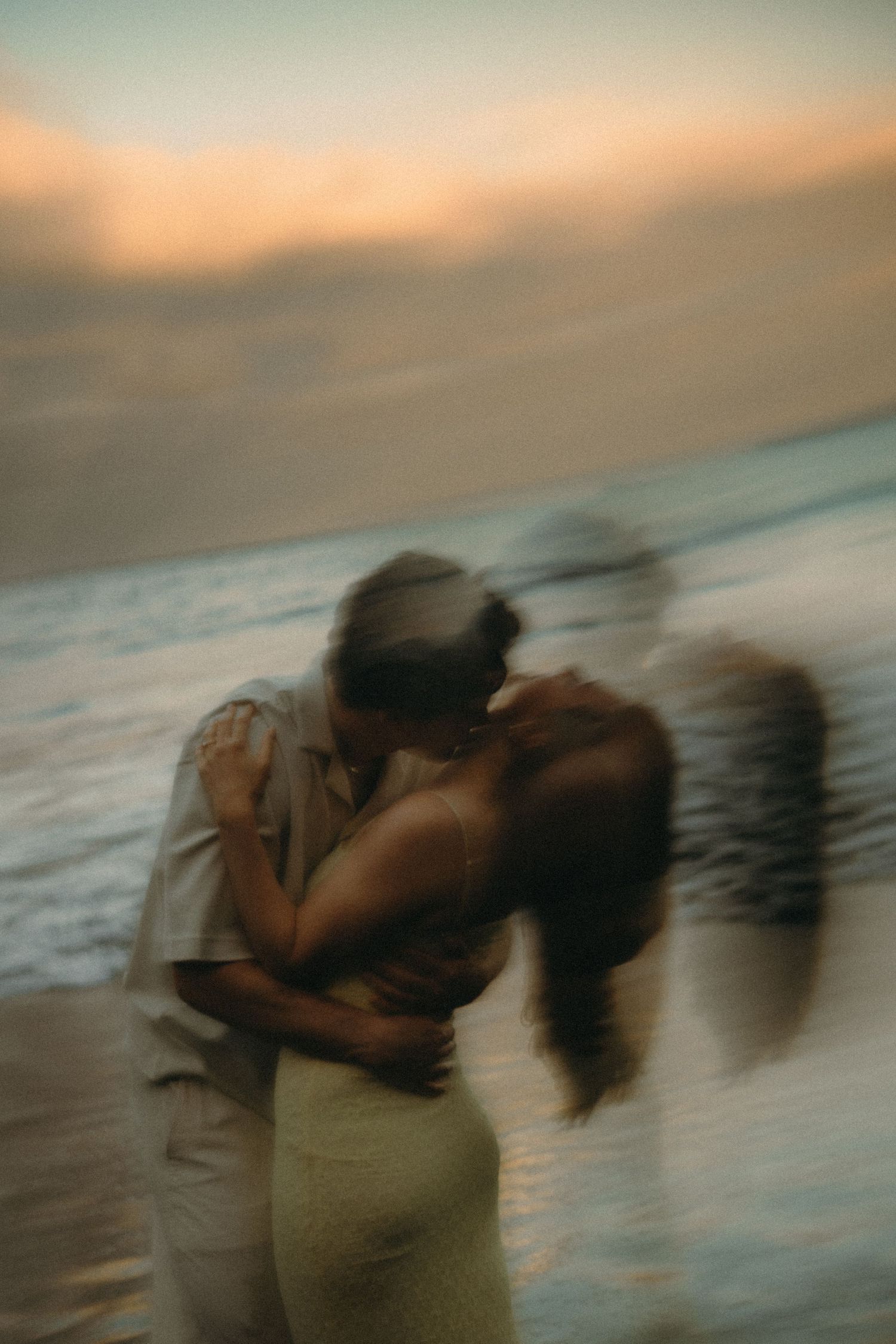 Blurry romantic couple kissing on beach at sunset, motion blur effect, ocean waves in background.